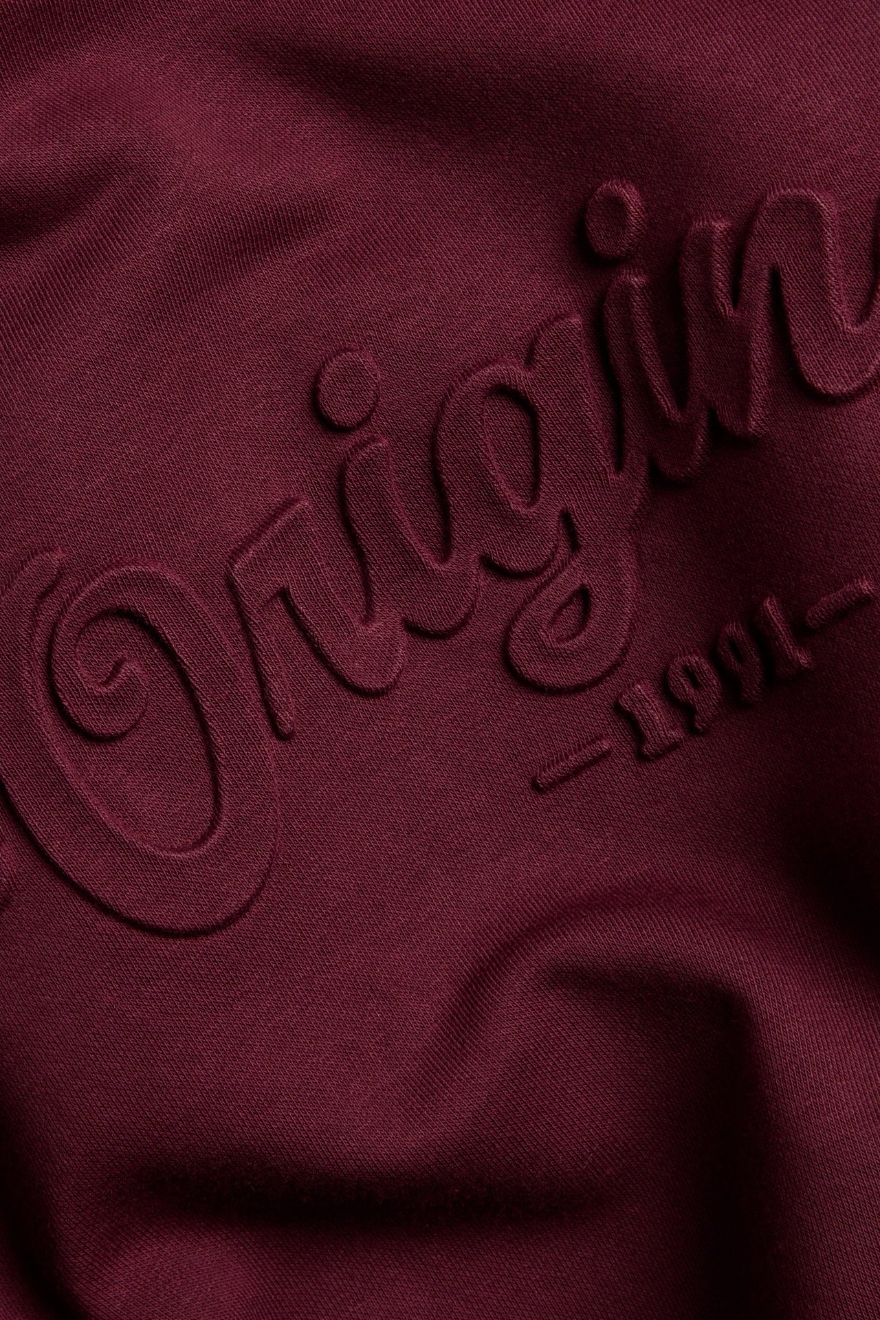 Zbliżenie na ciemnoczerwoną bluzę z efektem 3D i napisem 'Origin -1991-'.