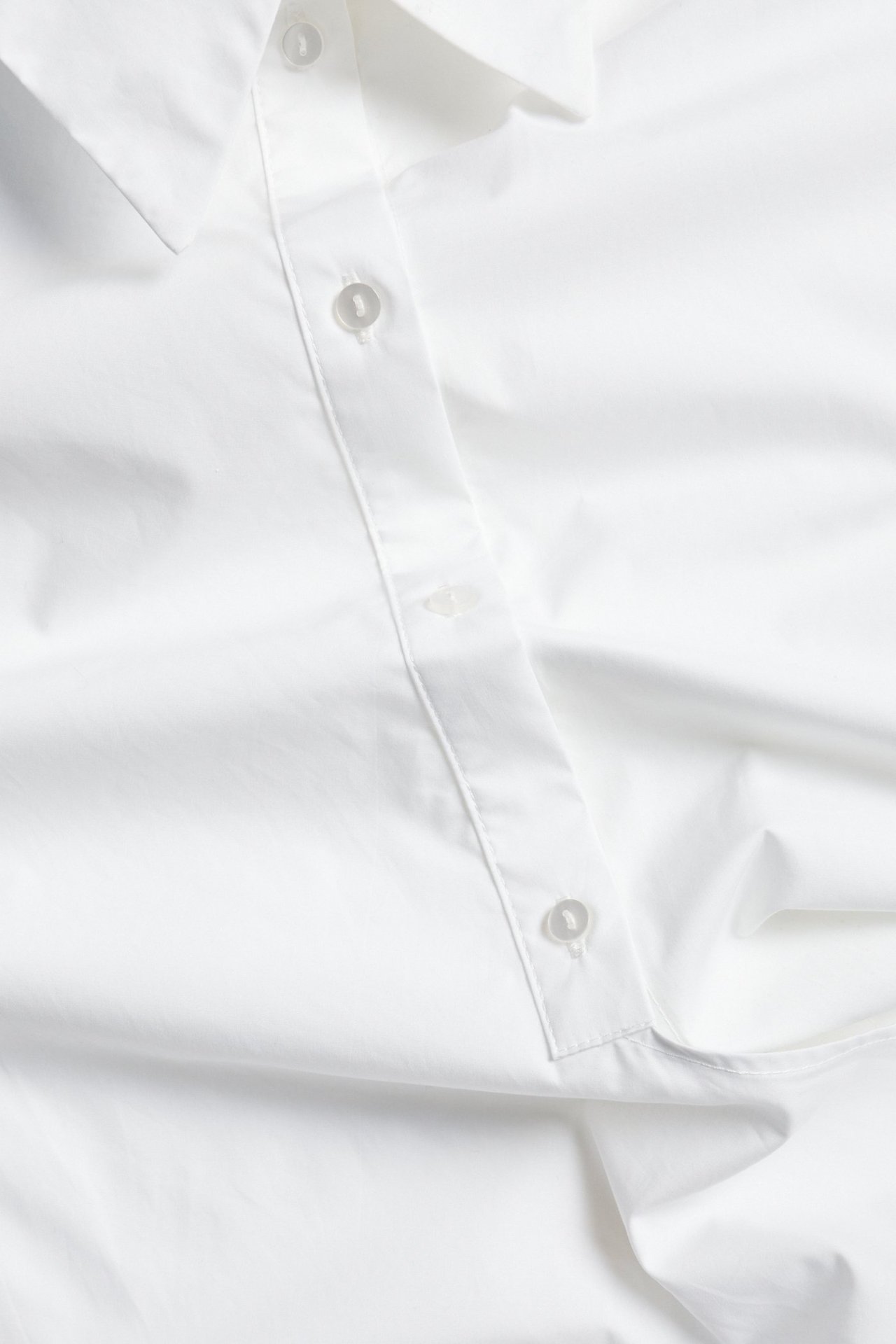 Zbliżenie białej bawełnianej koszuli z listwą guzikową i kołnierzykiem.