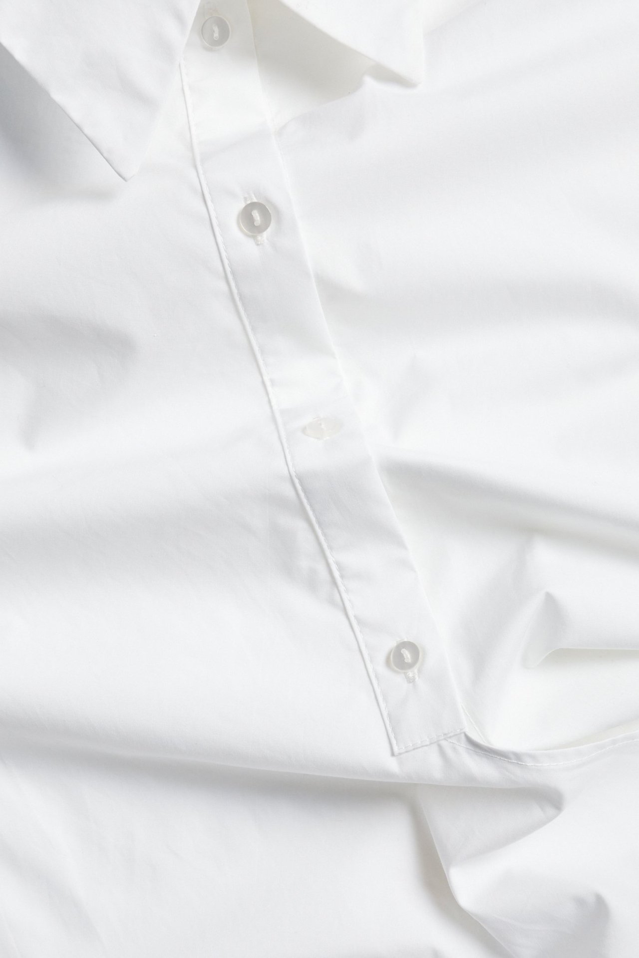 Lähikuva valkoisesta puuvillapaidasta, jossa napit ja klassinen kaulus.