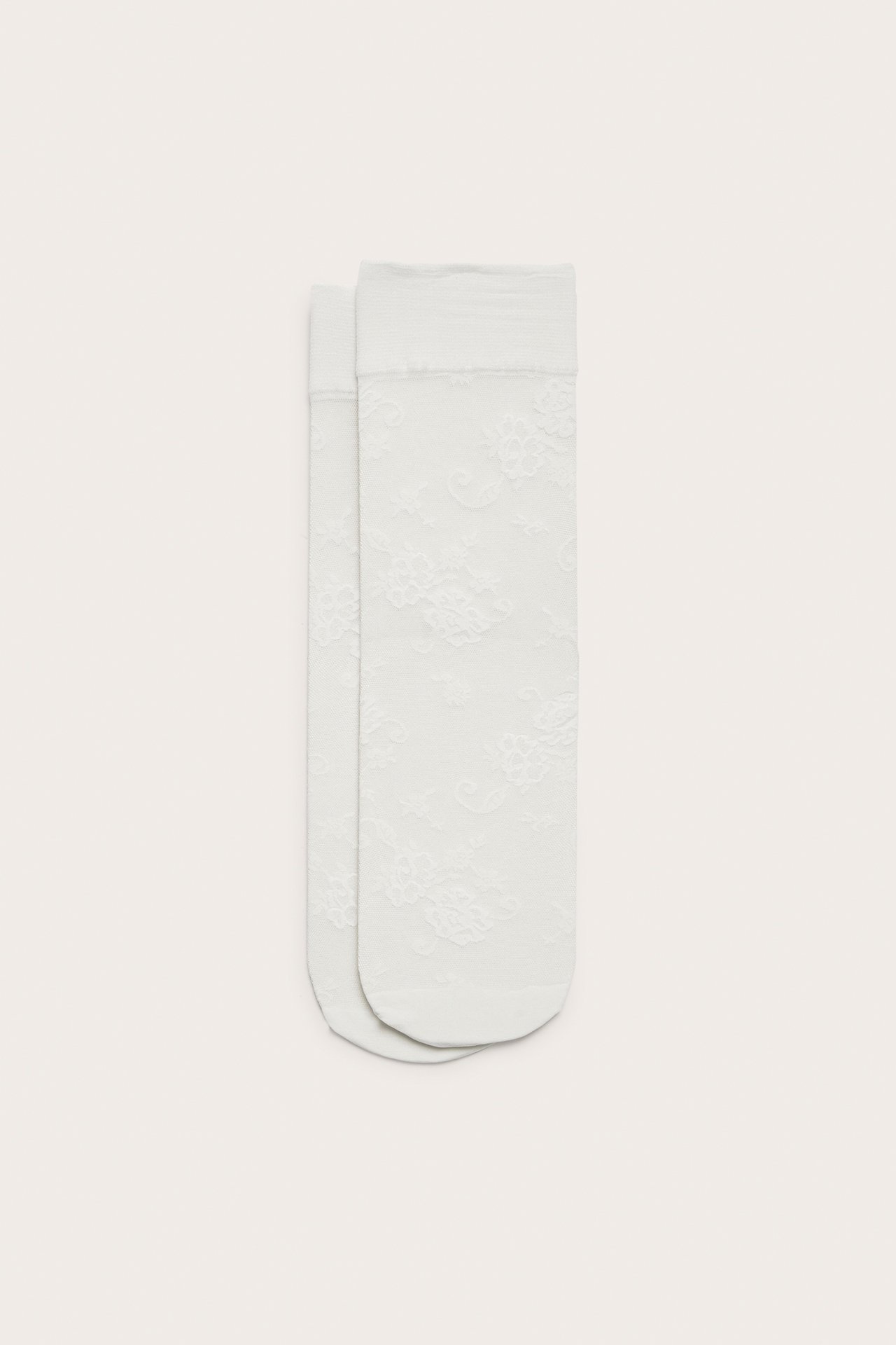 Uppifrån sett, två benvita tunna nylonsockor med delikat blommigt spetsmönster och ribbade muddar.