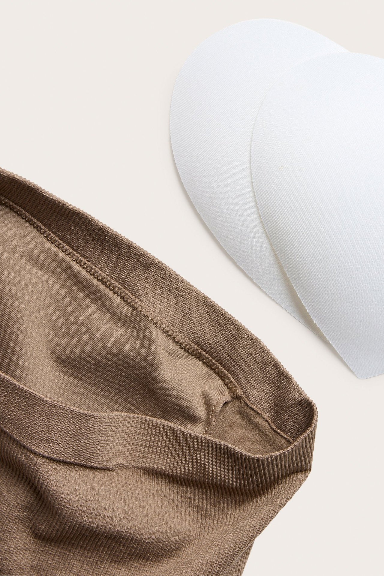 Zbliżenie beżowego, bezszwowego biustonosza bandeau i dwóch białych wkładek.