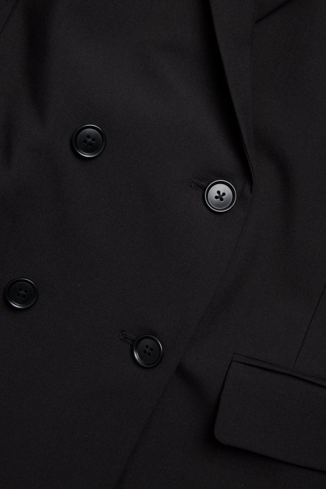 Zbliżenie czarnej dwurzędowej marynarki z czterema czarnymi guzikami i klapą kieszeni.