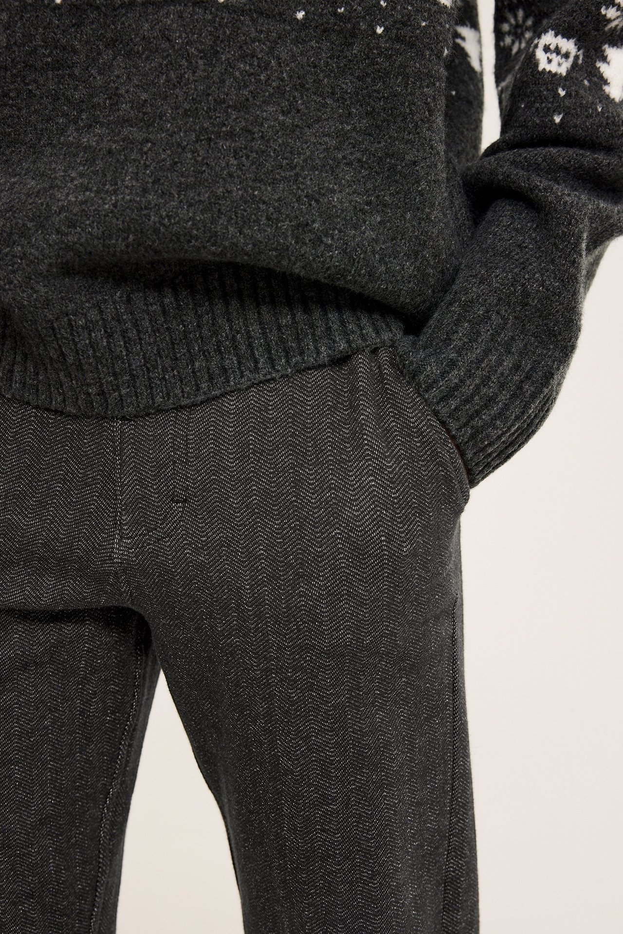 Lähikuva lapsesta, yllään tummanharmaat kalanruotokuosiset housut ja tummanharmaa kuvioneulottu neule.