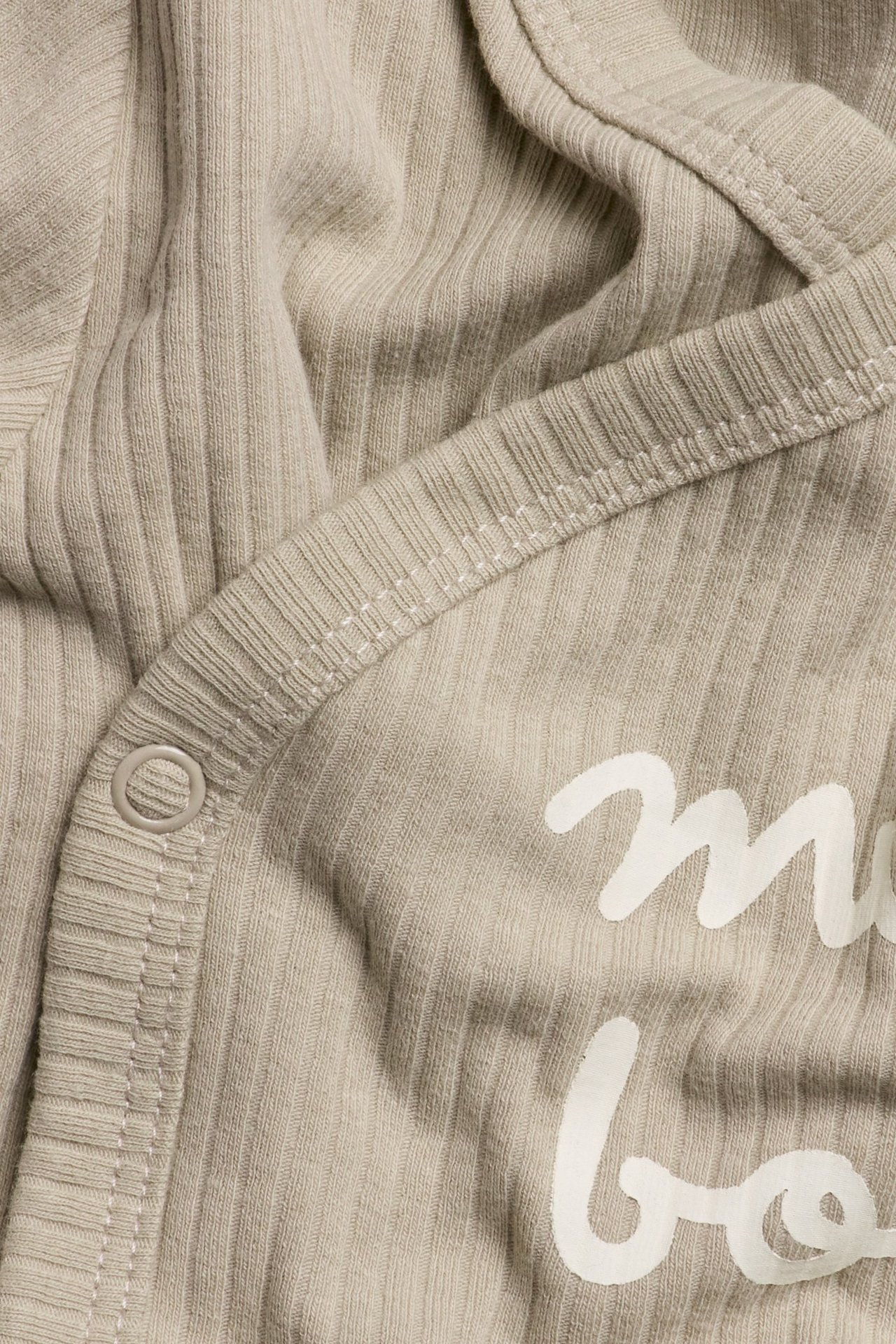 Zbliżenie na beżowe prążkowane body niemowlęce z zakładką na zatrzaski i białym nadrukiem.