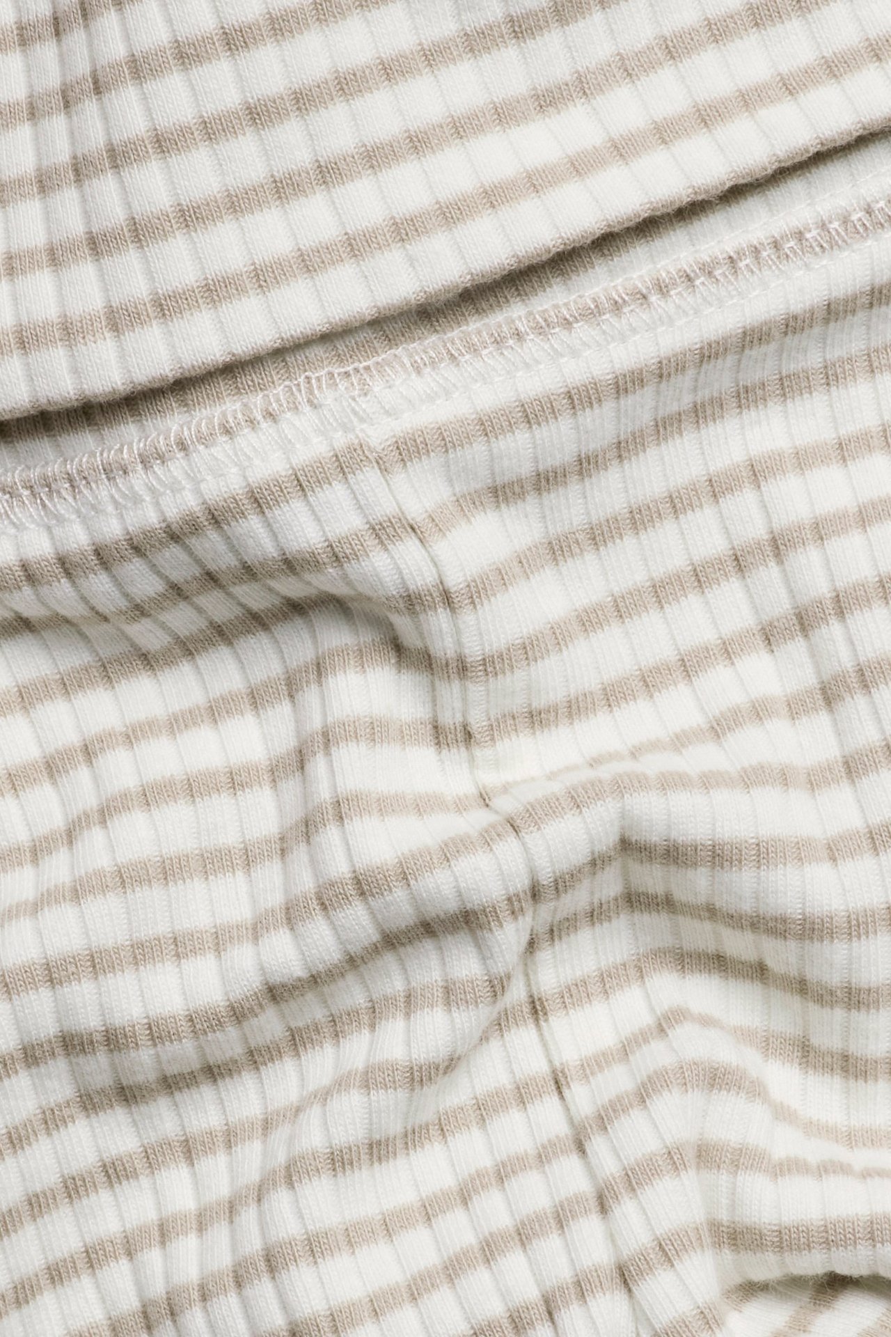Lähikuva offwhite- ja beigenvärisistä raidallisista ribbineuleisista vauvan leggingseistä, puuvillasekoitusta.