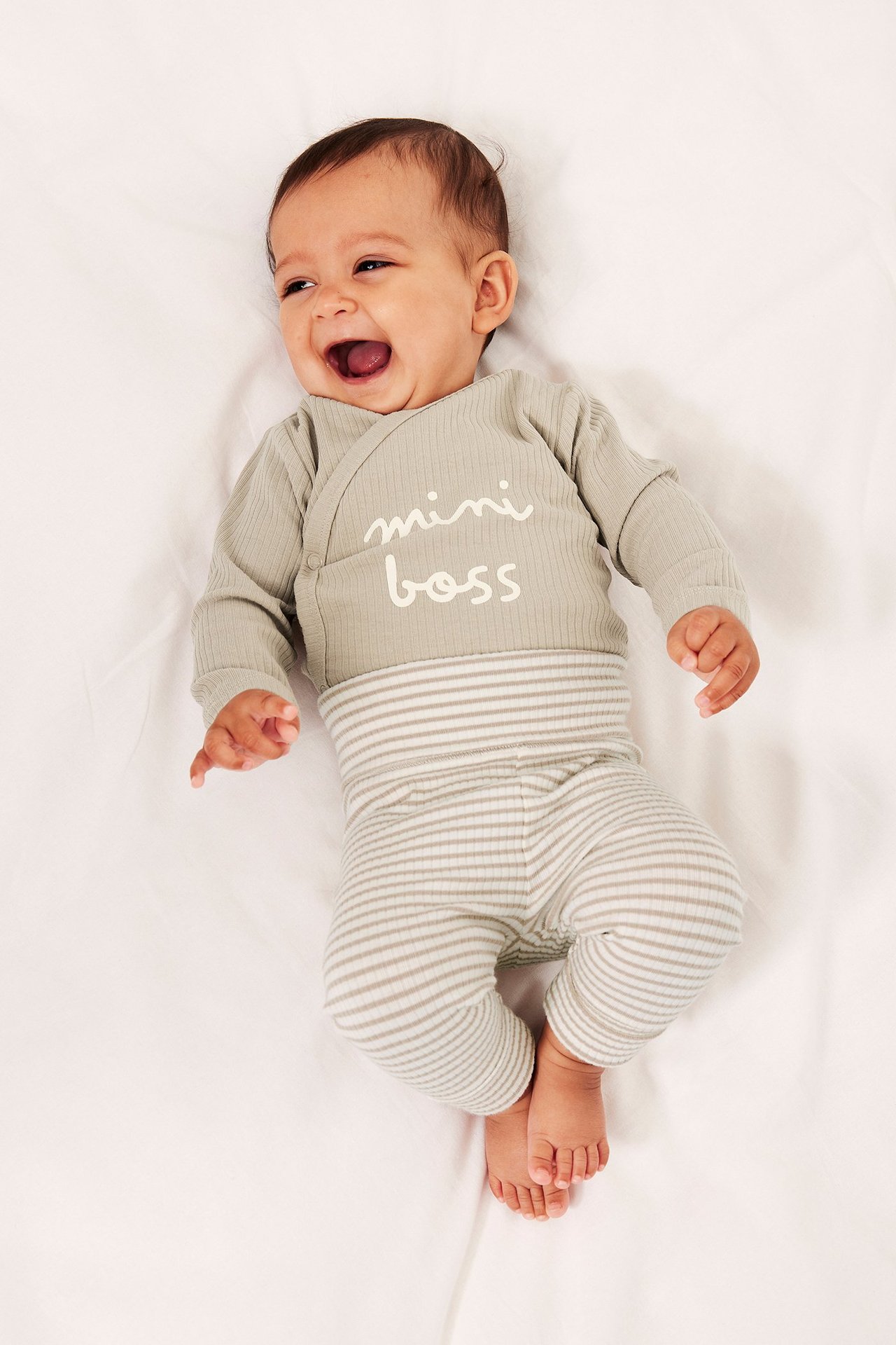 Ylhäältä kuvattu vauva yllään luonnonvalkoiset raidalliset ribbileggingsit ja vaaleanvihreä "mini boss" kietaisubody.
