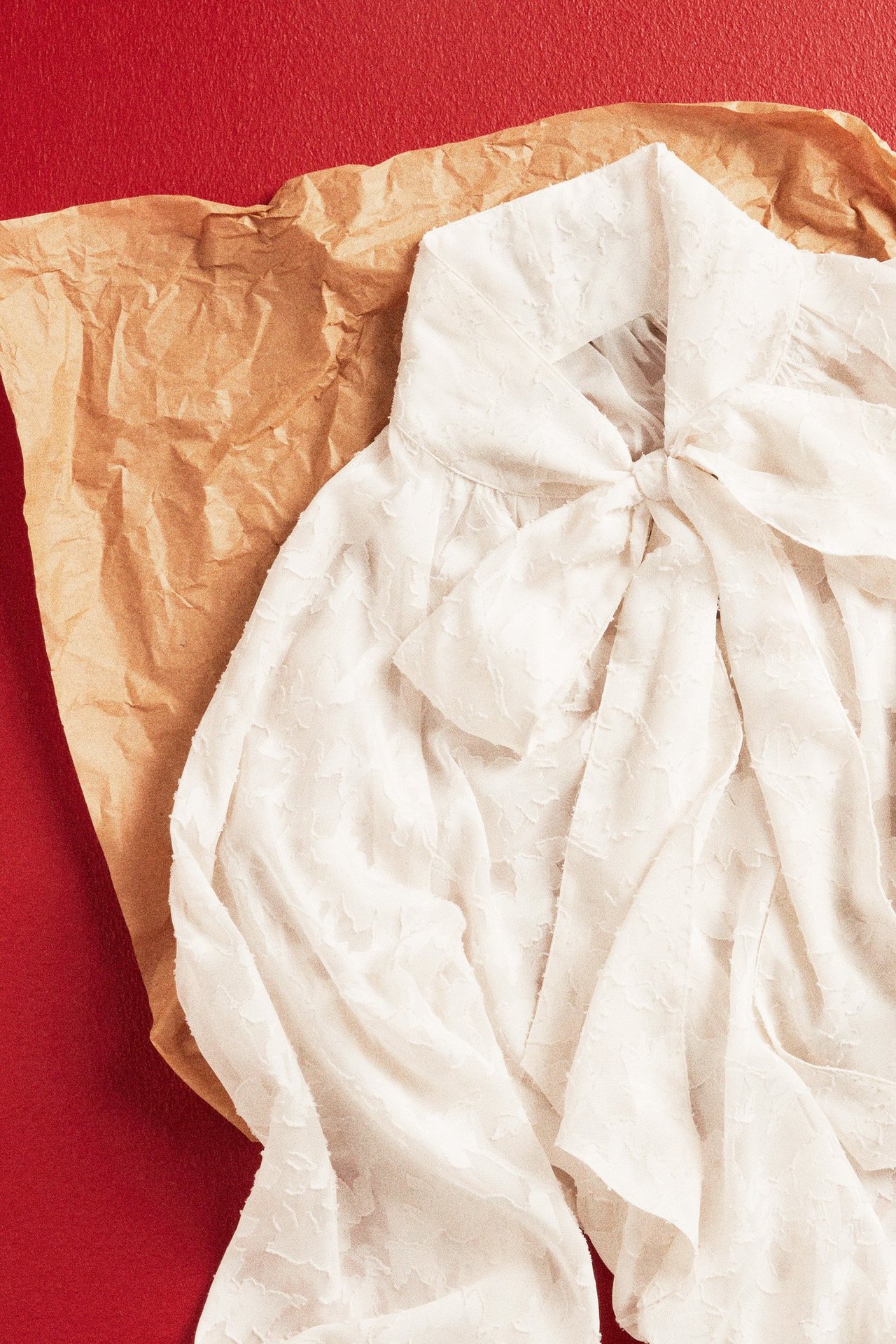 Platt läggning, uppifrån: Offwhite knytblus i strukturerad polyester med rosett vid kragen.