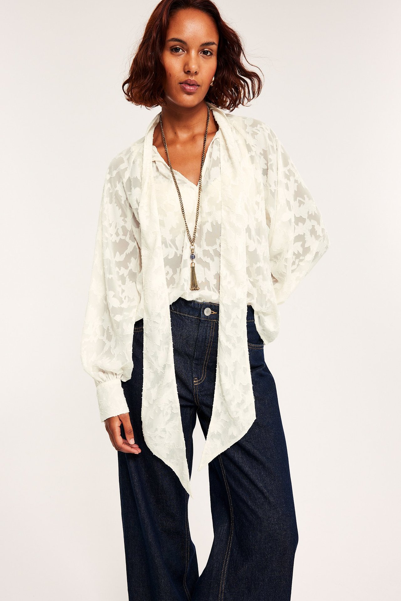 Kvinna i vit spetsblus med knyt runt halsen, långärmad, frontvy.