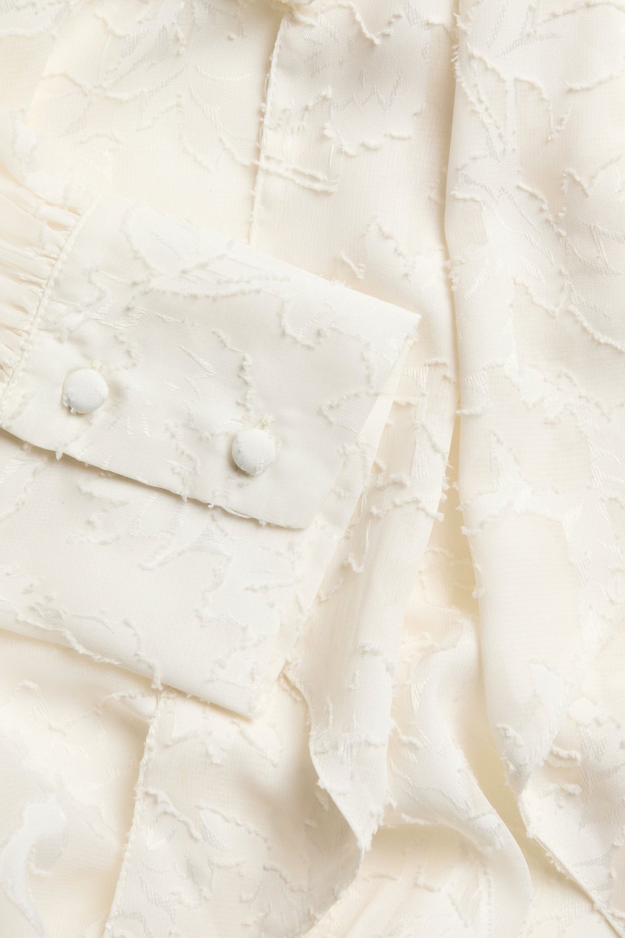 Zbliżenie na ecru koronkową bluzkę z poliestru, z fakturą i dwoma guzikami pokrytymi tkaniną na mankiecie.