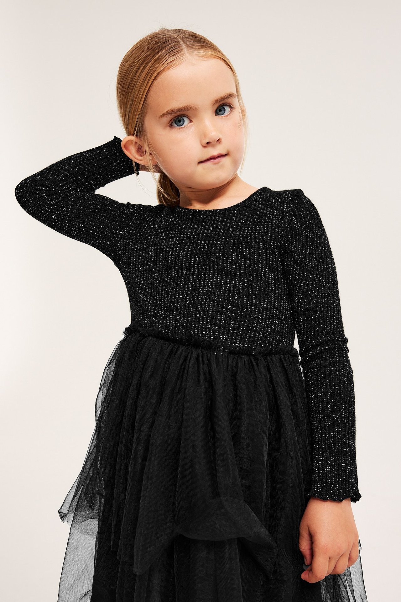 Etunäkymä lapsesta, joka käyttää mustaa kimaltavaa ribbimekkoa, jossa on kerroksellinen tyllihame.