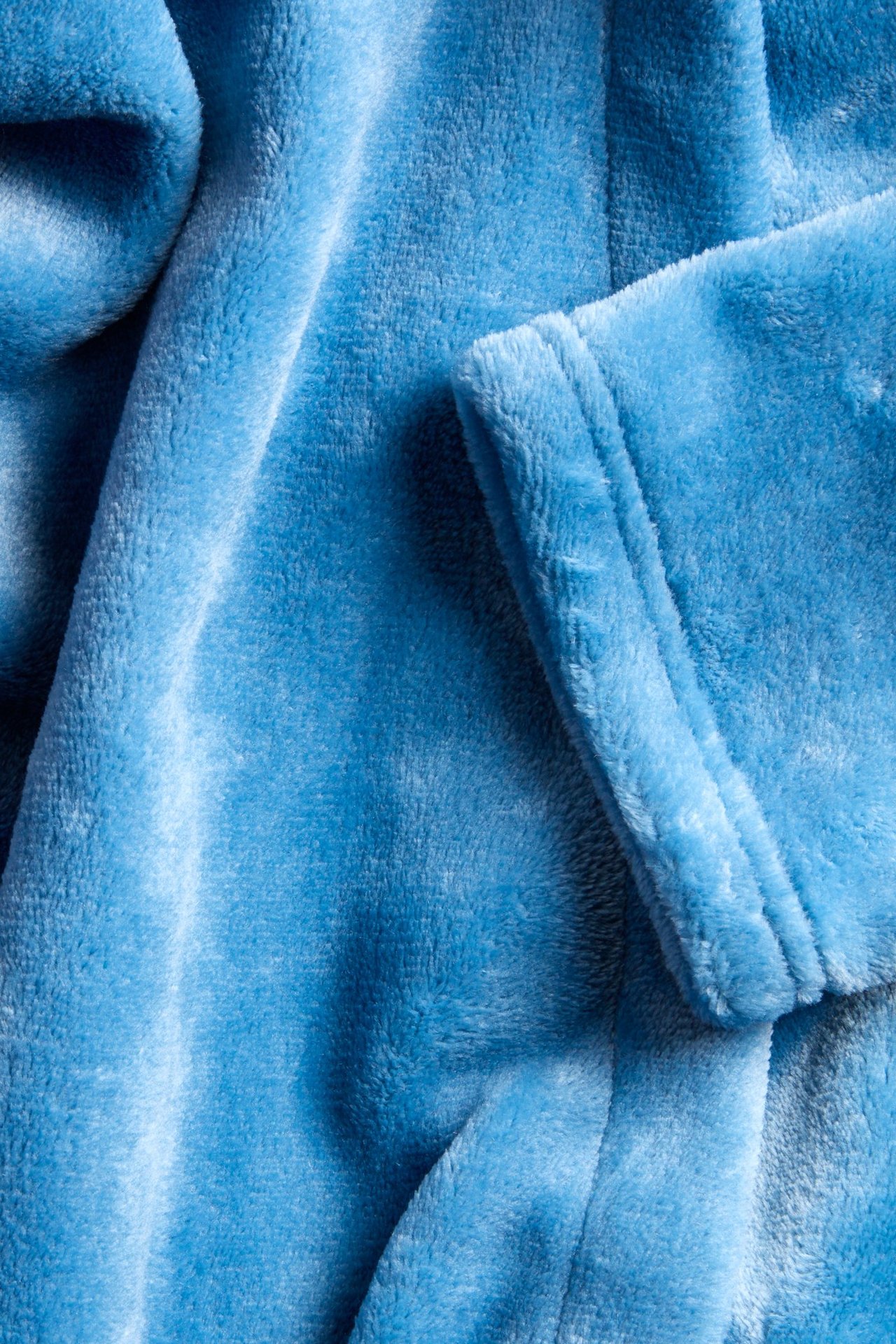 Zbliżenie na niebieski szlafrok polarowy, ukazujące jego miękki, teksturowany materiał i złożony mankiet rękawa.