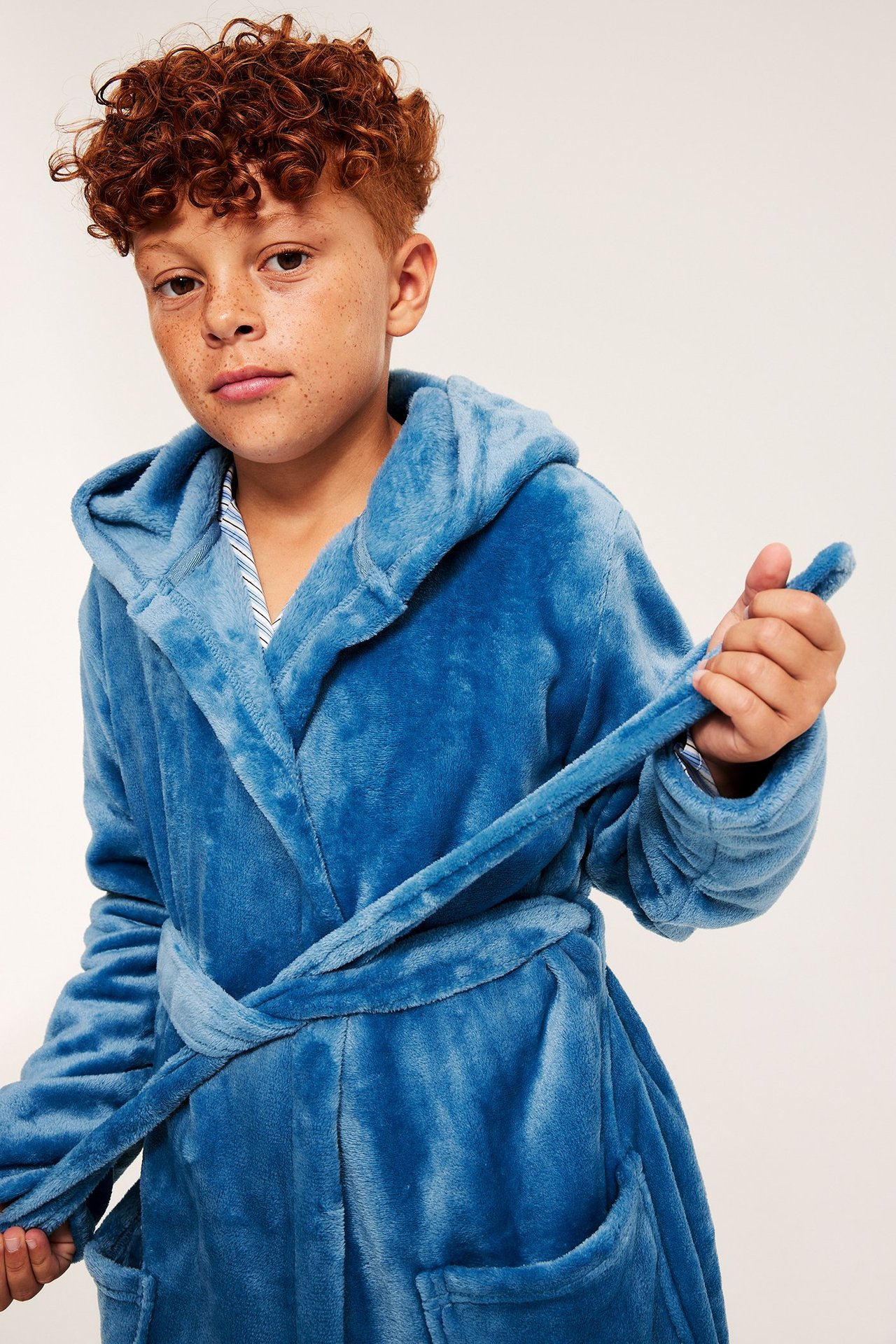 Edestä näkymä lapsesta, yllään sininen hupullinen fleece-kylpytakki, taskut ja vyö, raidallisen paidan päällä.
