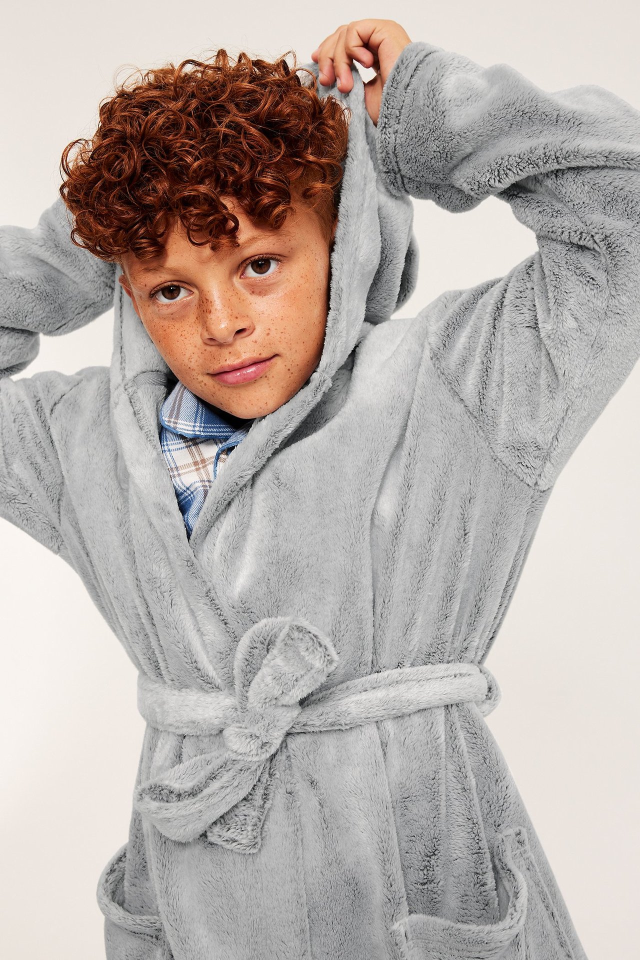 Zbliżenie dziecka w szarym, melanżowym szlafroku polarowym z kapturem, z wiązanym paskiem, na koszuli w kratę.