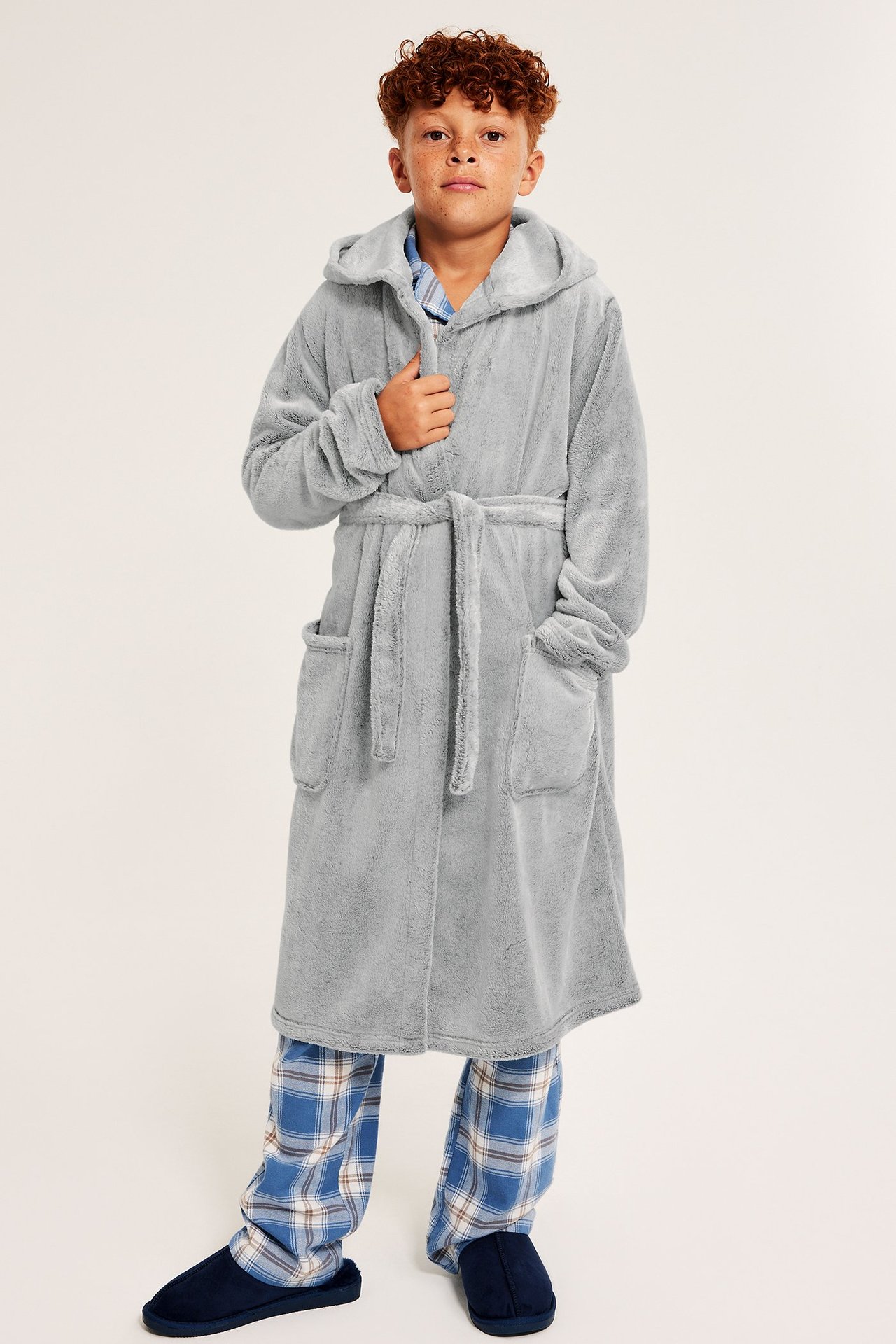 Widok z przodu, dziecko w szarym, melanżowym, polarowym szlafroku z kapturem, piżamie w kratę i granatowych kapciach.