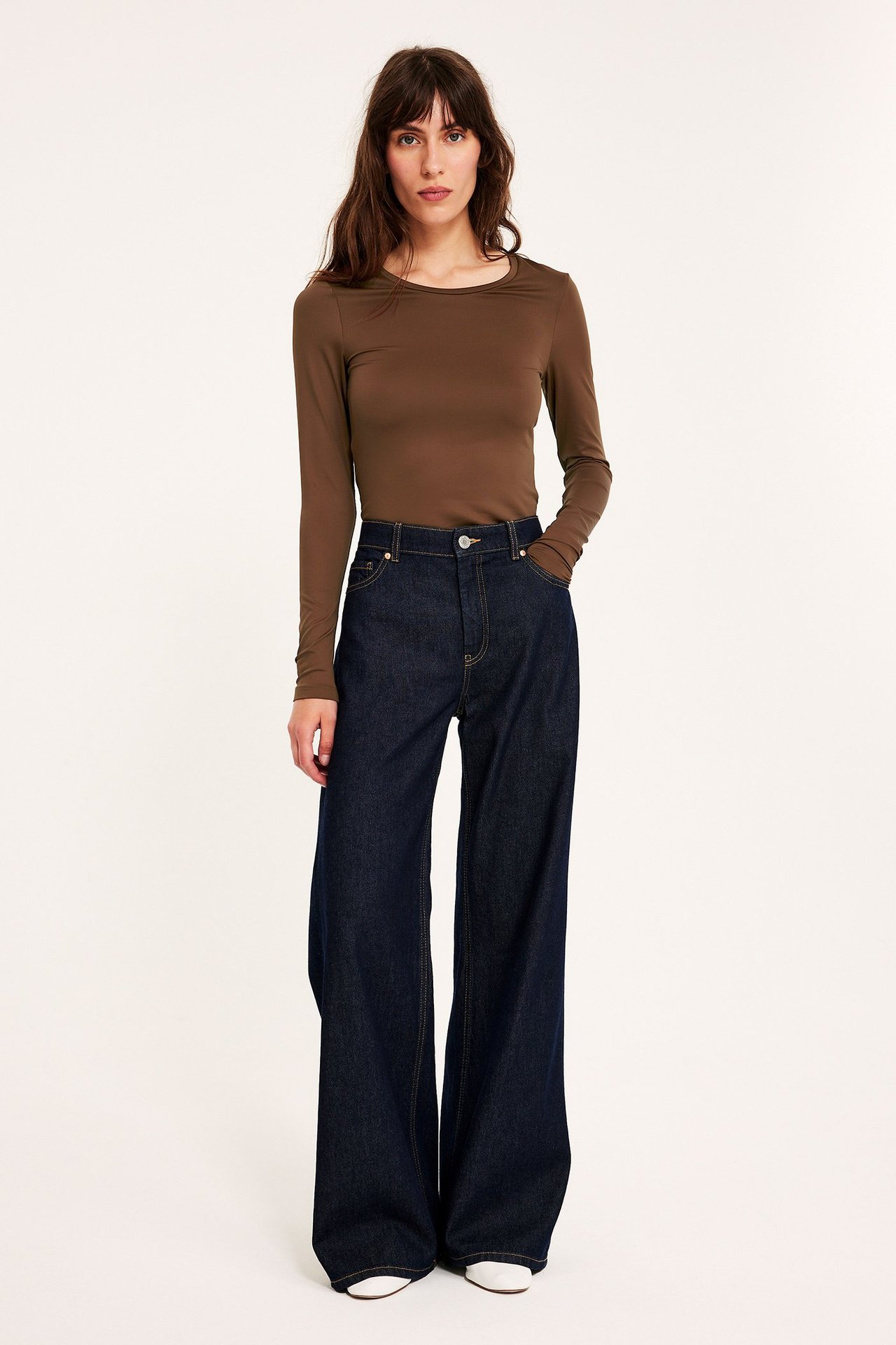 Forfra: kvinne i brun langermet rundhalset topp og mørkeblå vide jeans.