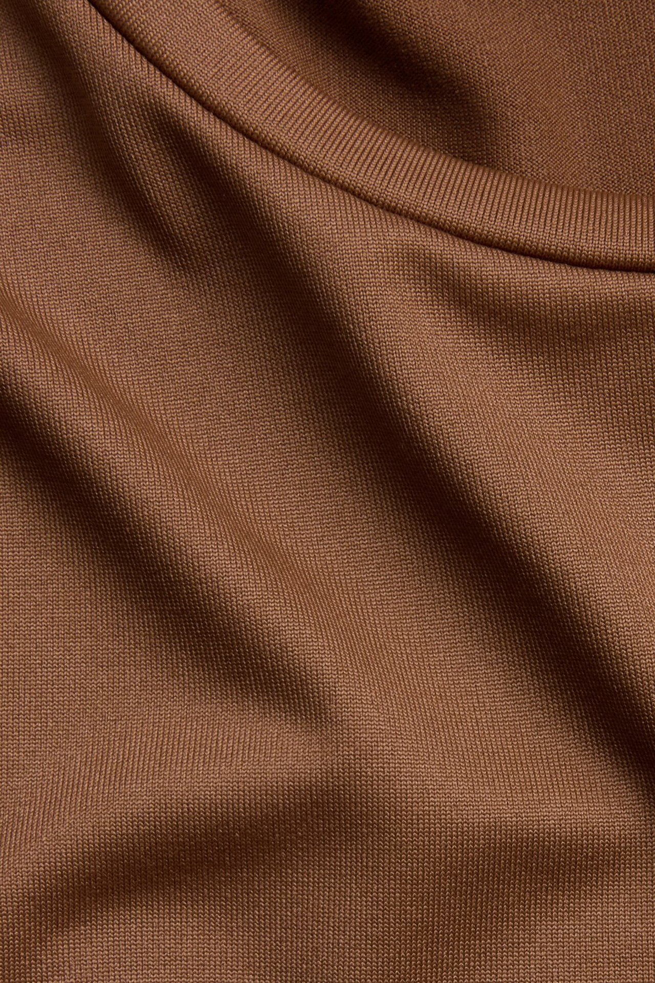 Zbliżenie brązowego topu z długim rękawem, o prążkowanej fakturze i okrągłym dekolcie.