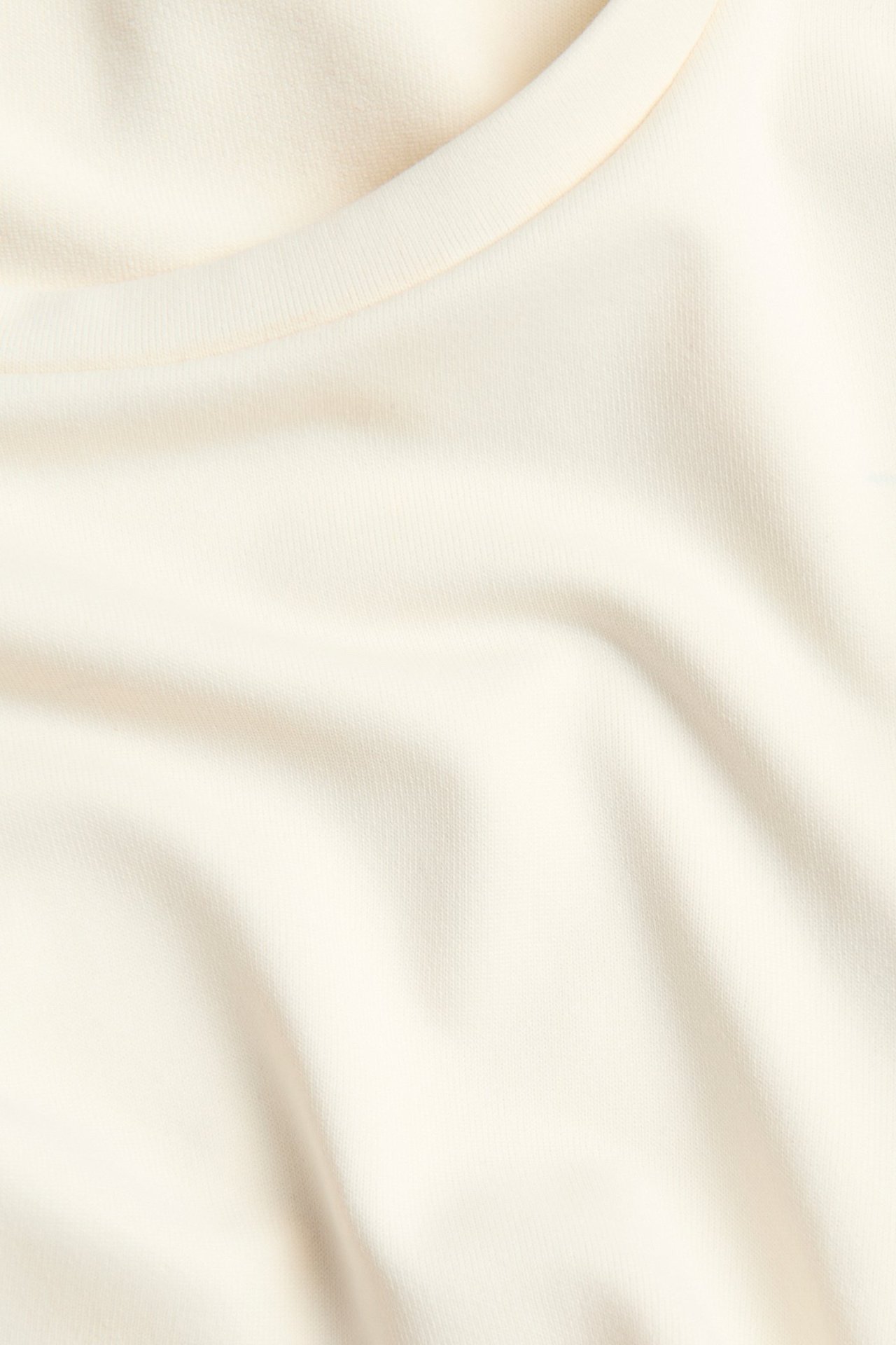 Zbliżenie na kremowy top z długim rękawem i okrągłym dekoltem, ukazujące miękką fakturę materiału.
