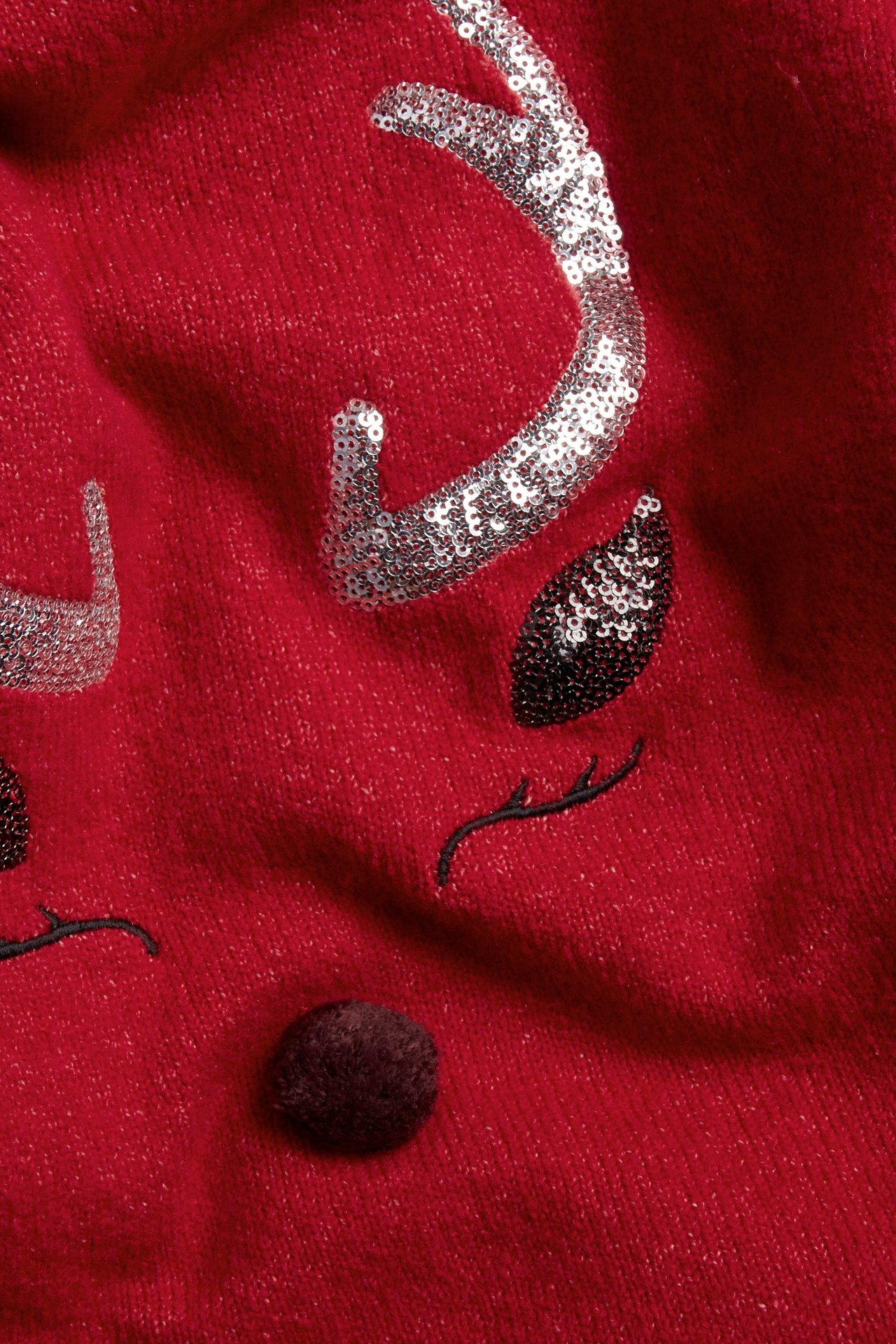 Zbliżenie: czerwony dzianinowy sweter z aplikacją renifera, srebrnymi cekinowymi rogami, czarnymi oczami, brązowym noskiem.