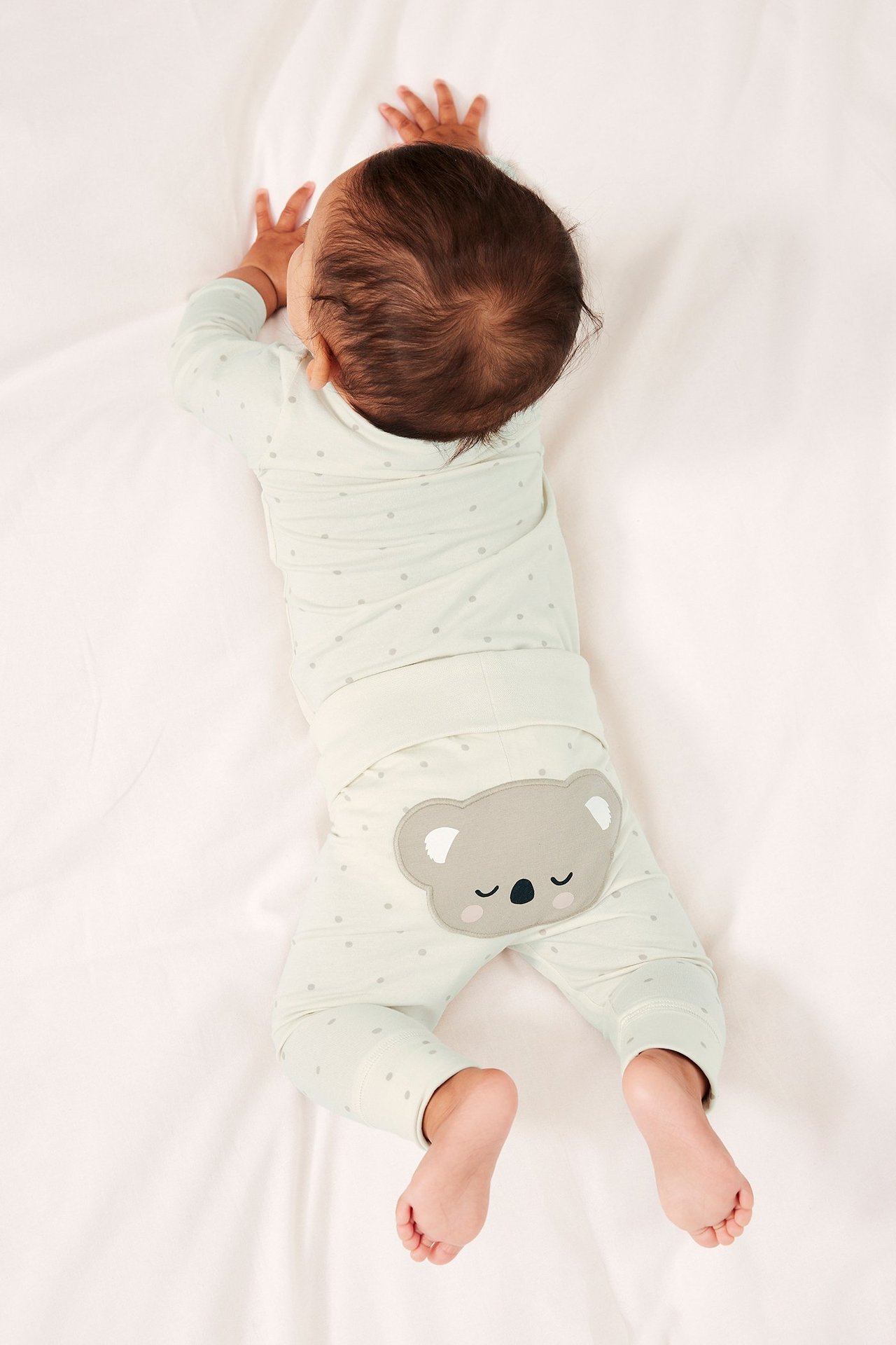 Ylhäältä kuvattu vauva yllään luonnonvalkoinen kuvioitu body ja leggingsit koala-applikaatiolla.