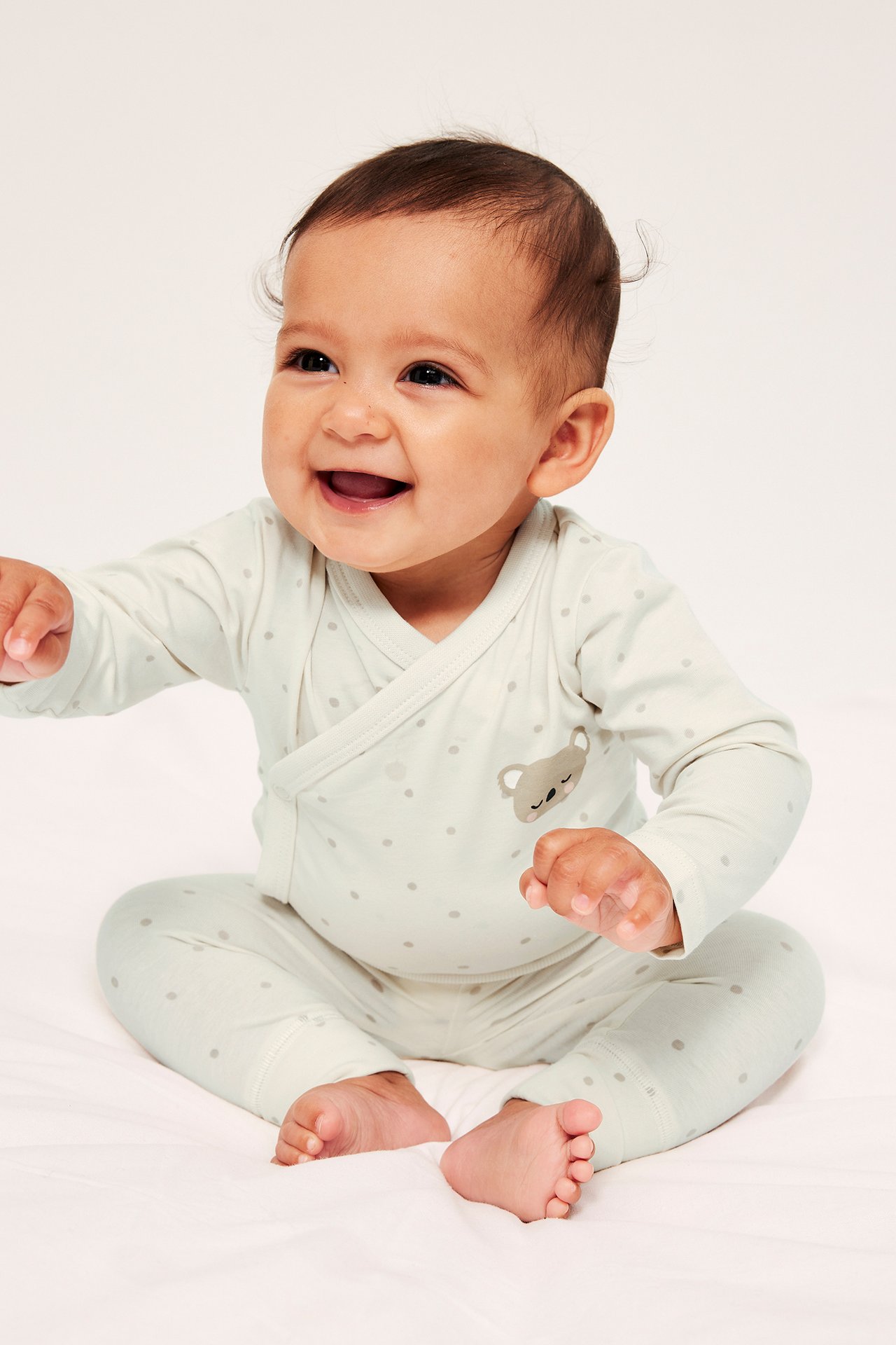 Framsida av en baby i en offwhite mönstrad omlottbody med koalatryck och matchande leggings.