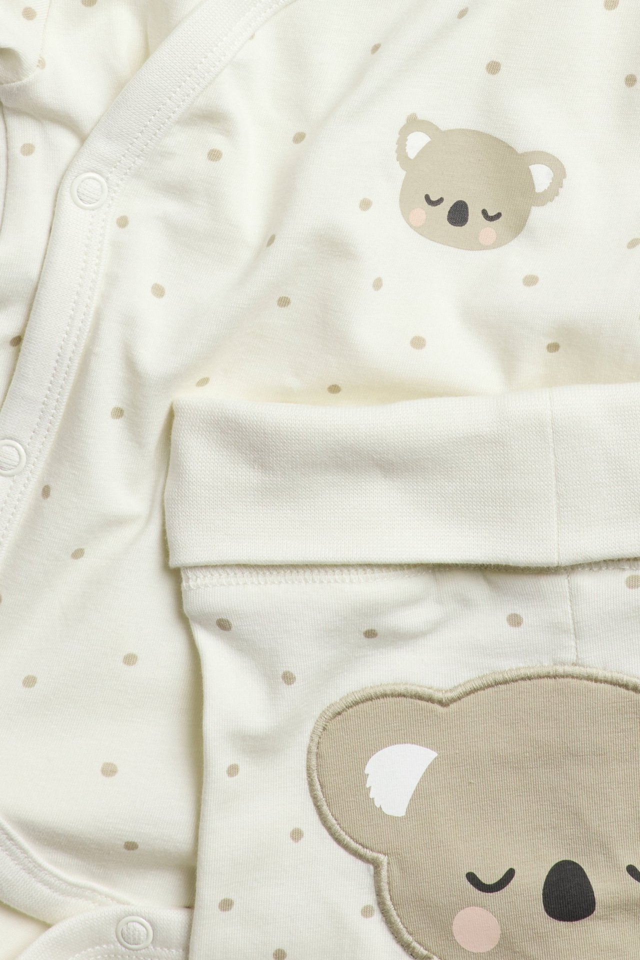 Zbliżenie na kremowy dwuczęściowy zestaw niemowlęcy w beżowe kropki i motywy koali.