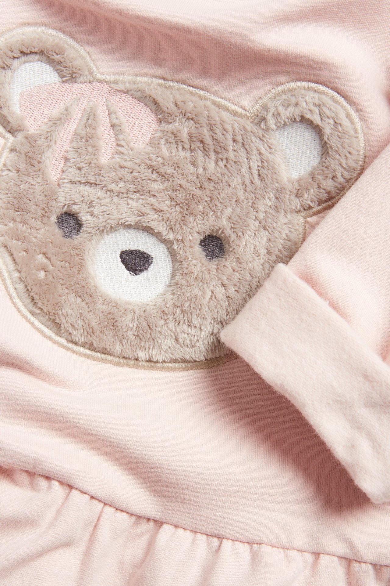 Zbliżenie z przodu różowej bluzy niemowlęcej z puszystą brązową aplikacją misia i falbanką.