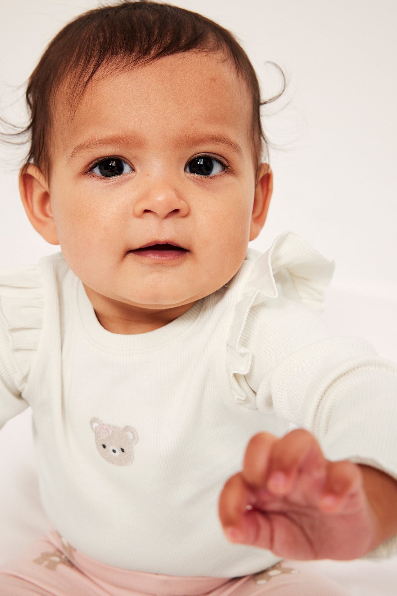 Lähikuva vauvasta yllään luonnonvalkoinen ribattu body olkarypytyksillä ja nallekirjonnalla.