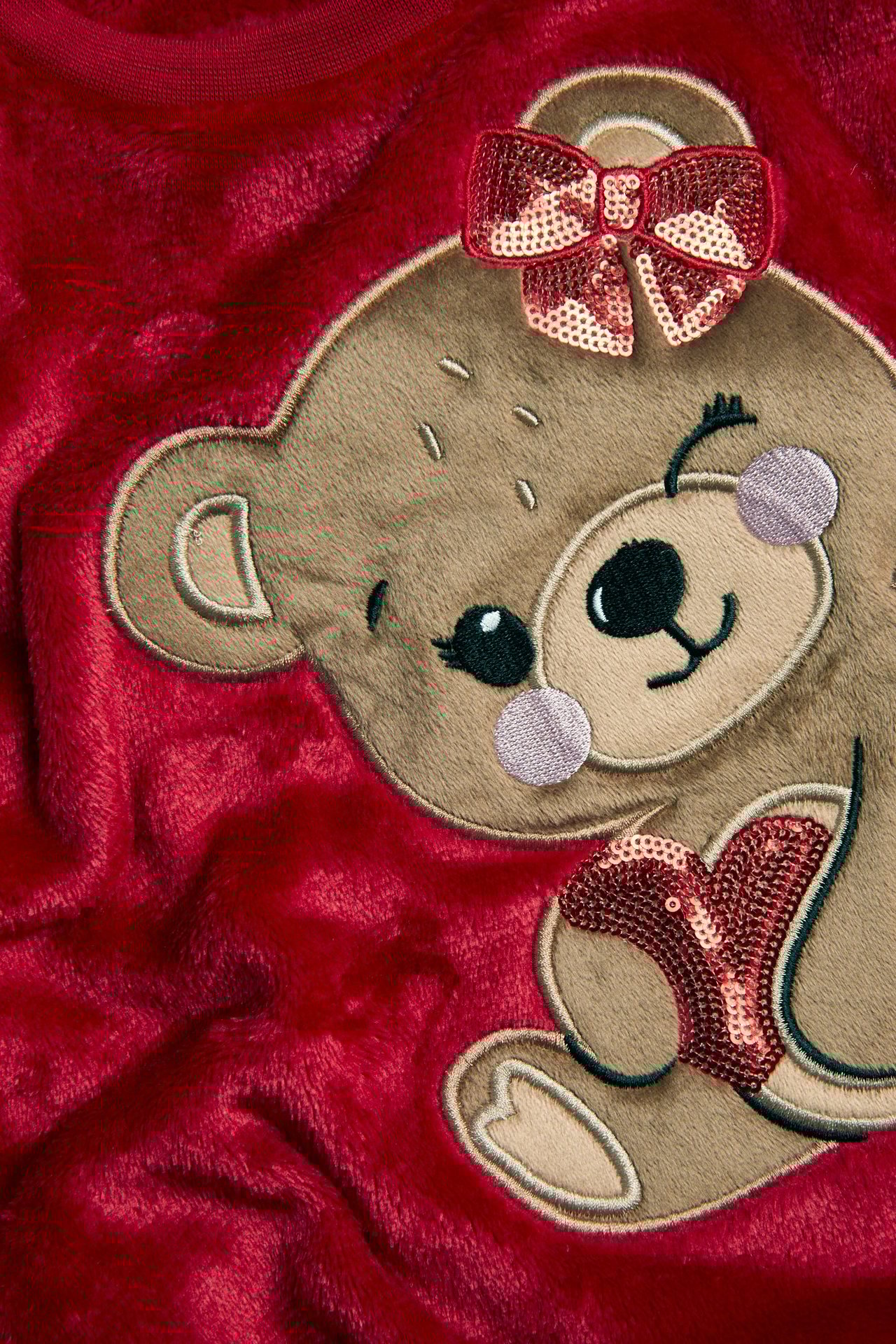Zbliżenie na czerwoną, puszystą bluzę z haftowanym misiem, kokardą i sercem z cekinów.