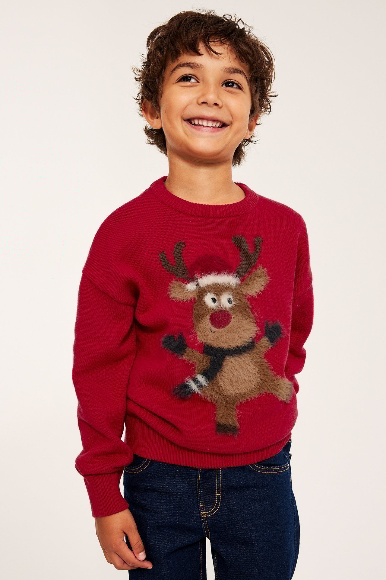 Dziecko w czerwonym swetrze bożonarodzeniowym z aplikacją Rudolfa, dzianina na karku i rękawach.