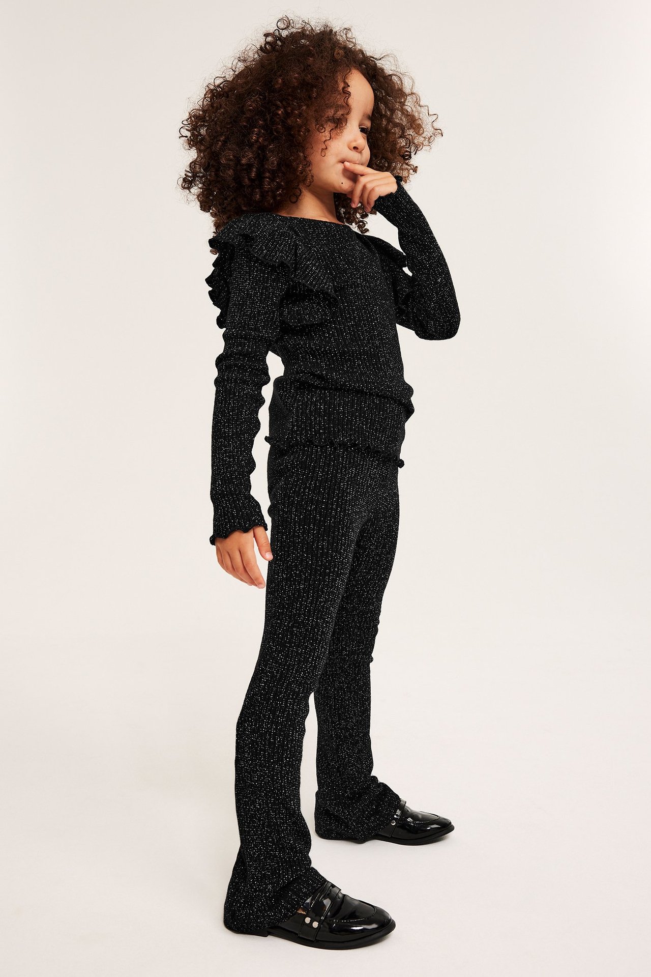 Widok z boku: dziecko w czarnych, błyszczących legginsach flare, pasującym topie i mokasynach.