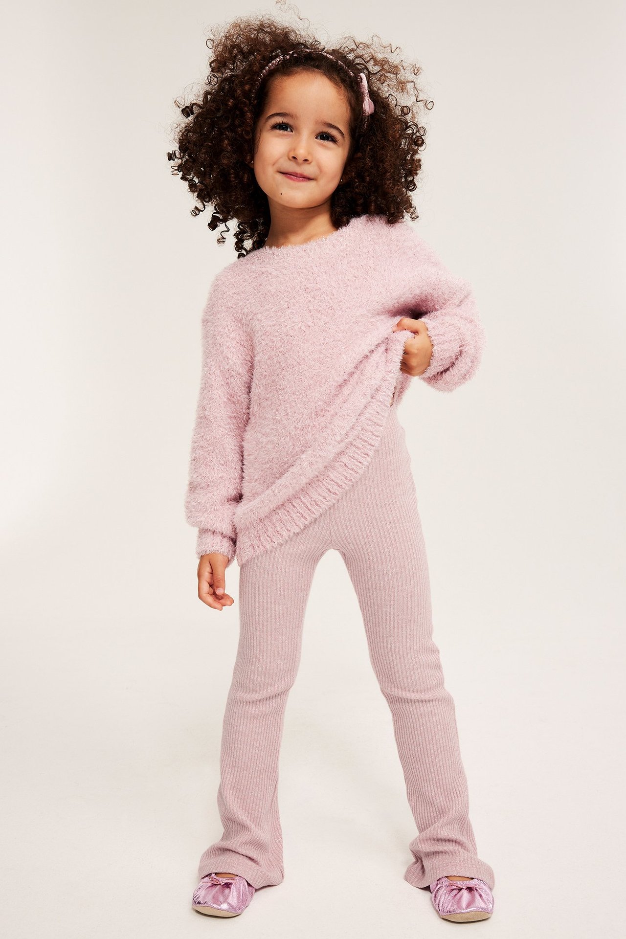 Edestä: Lapsi yllään vaaleanpunaiset kimalle ribbileggingsit, pörröinen neule ja vaaleanpunaiset ballerinat.