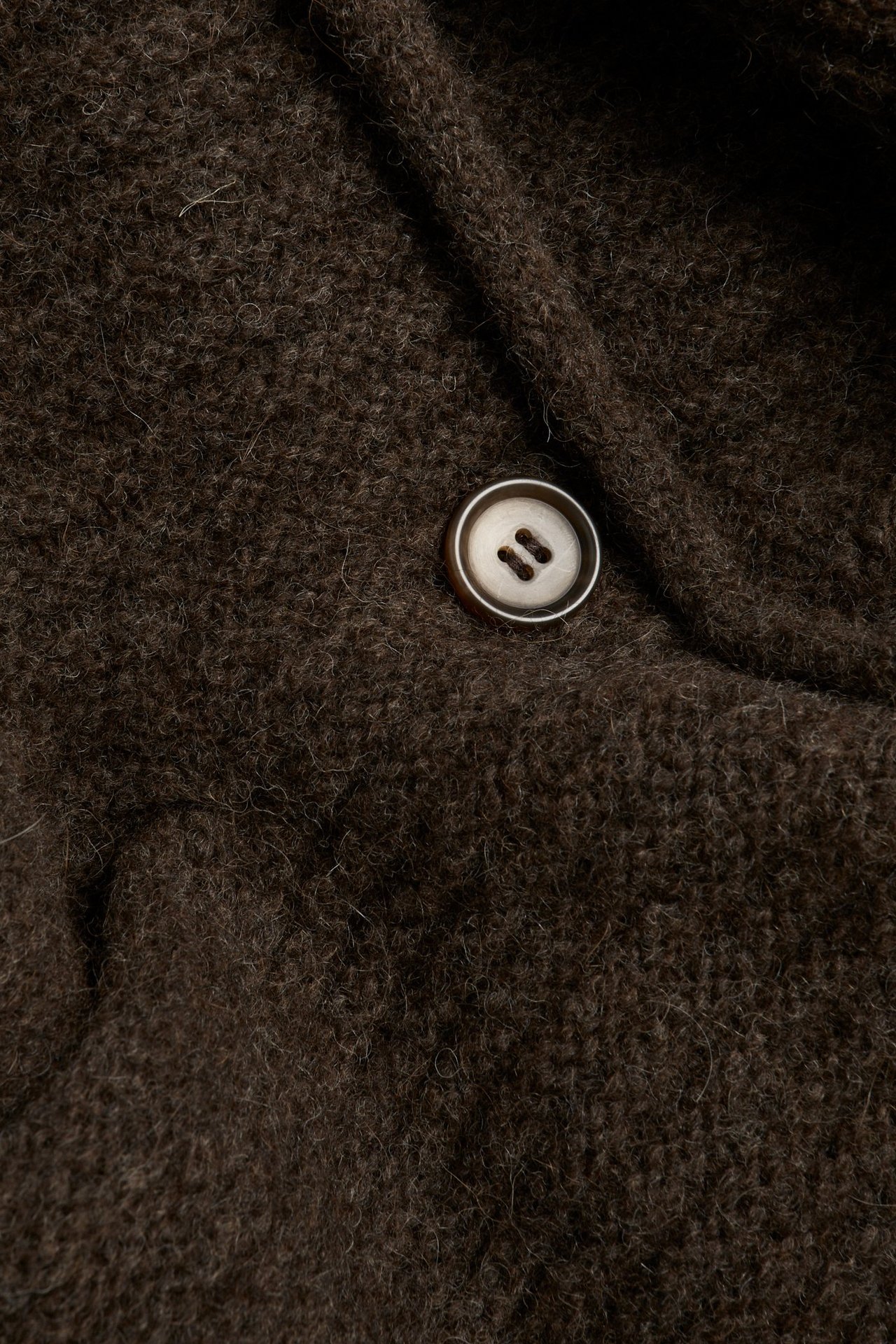 Zbliżenie na ciemnobrązowy melanżowy dzianinowy kardigan z mieszanki wełny z jasnym guzikiem.