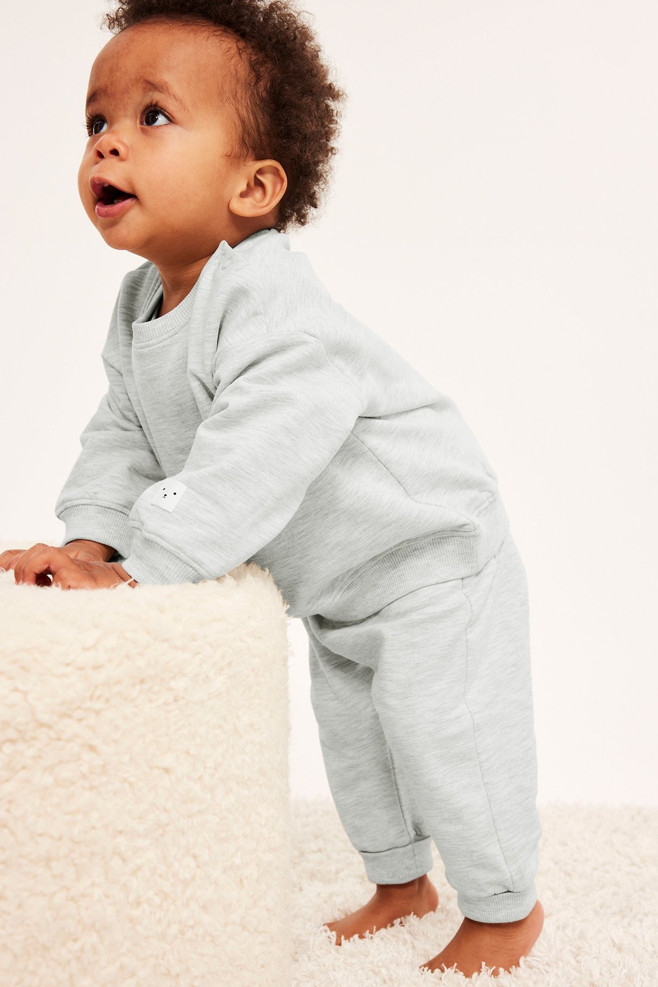 Sidovy av en baby i gråmelerad sweatshirt med axelknappar och matchande byxor.