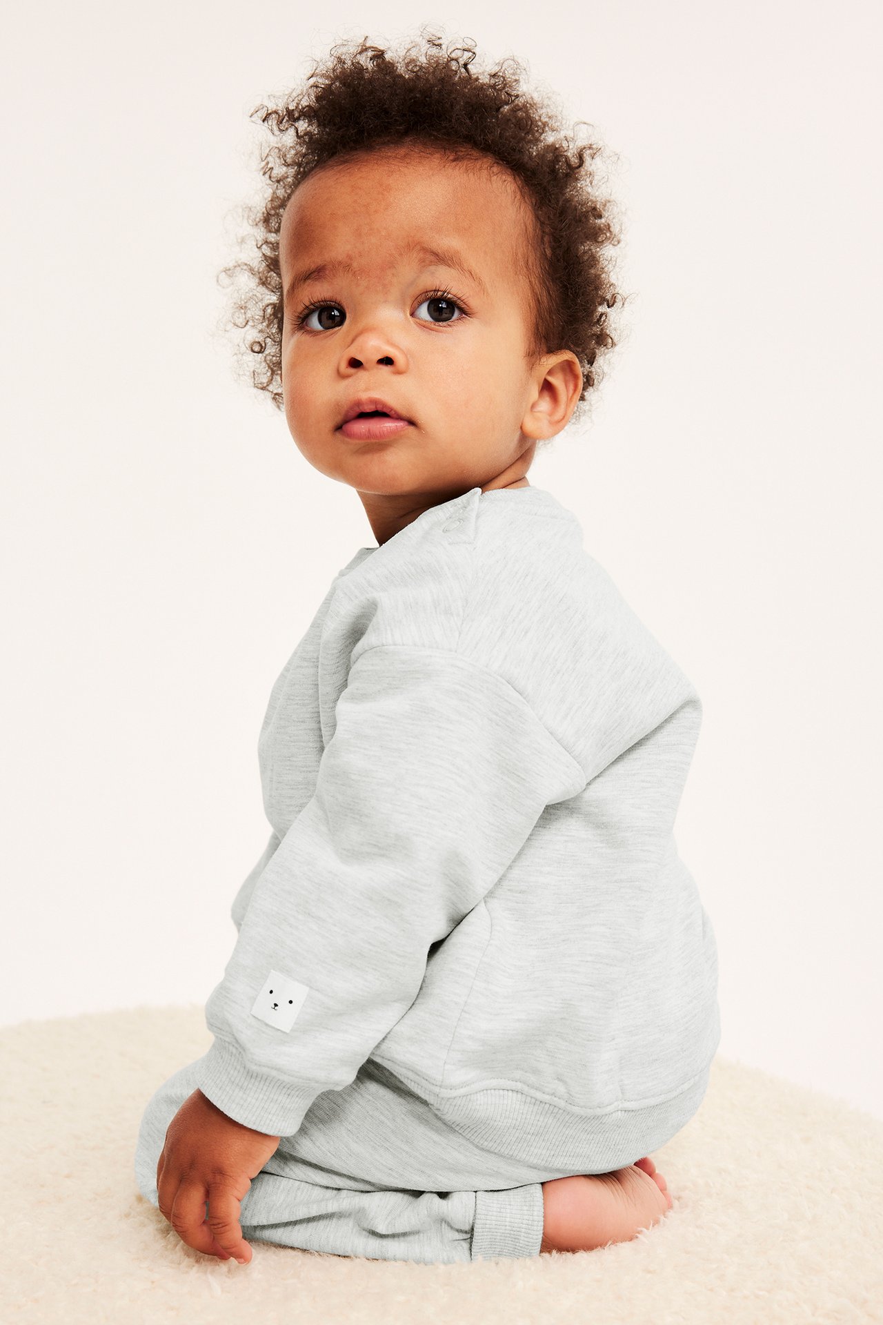 Sidebilde av en baby i melert grå bomullssweatshirt med trykknapper og matchende bukse.