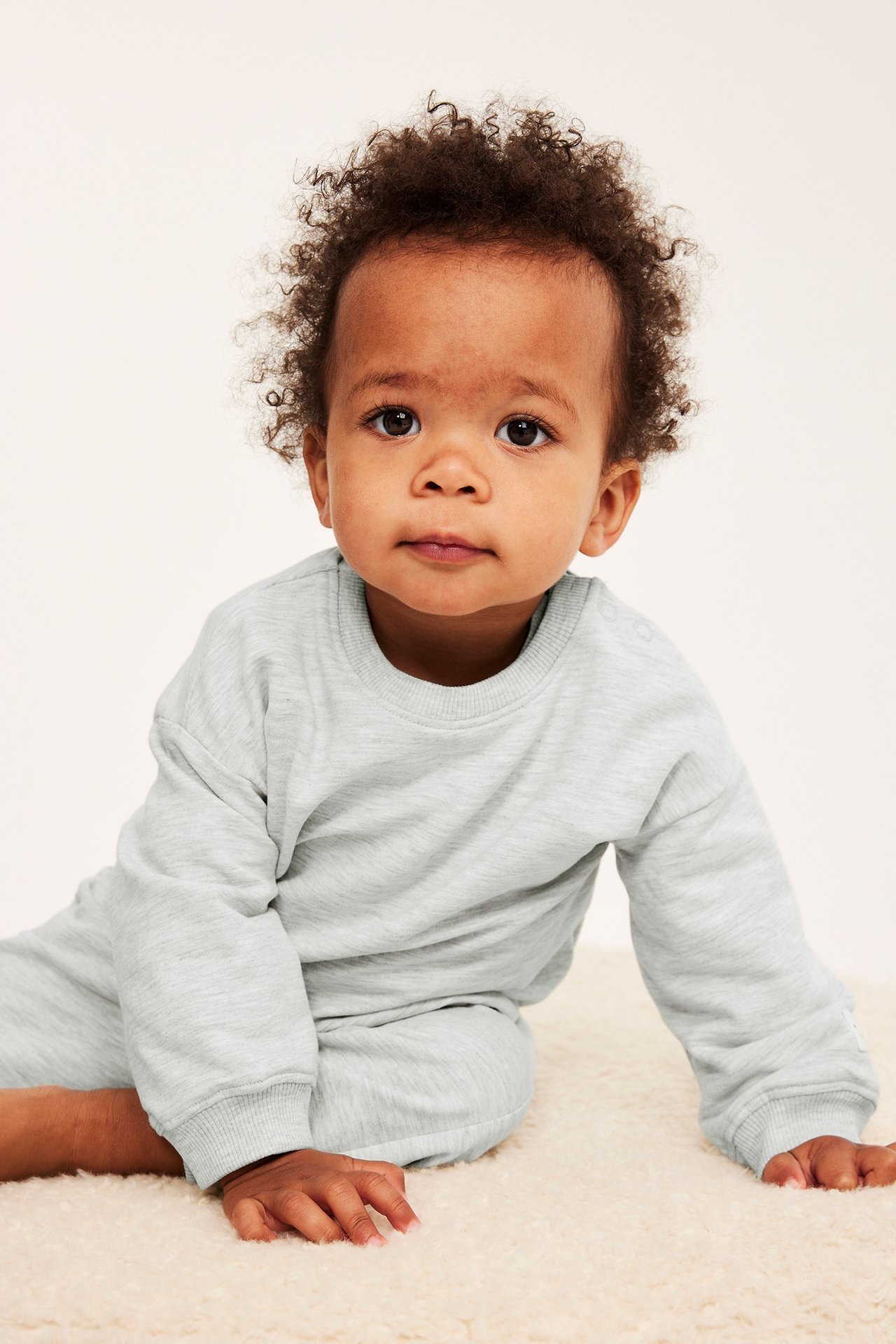 Frontvy av en baby i en melerad grå långärmad sweatshirt med tryckknappar och matchande byxor.