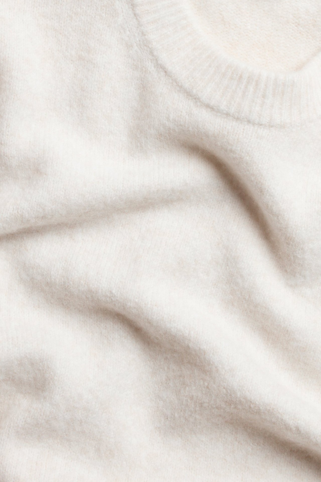 Zbliżenie jasnobeżowego, oversize'owego swetra z dzianiny z prążkowanym dekoltem.