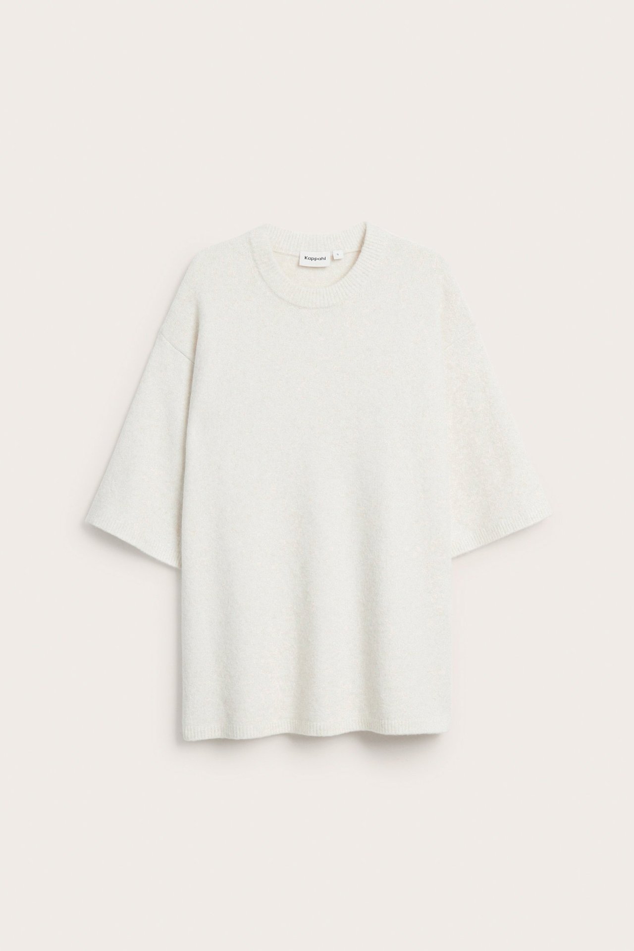 Z przodu: jasnobeżowy, jednolity, długi sweter oversize z okrągłym dekoltem i krótkimi szerokimi rękawami.