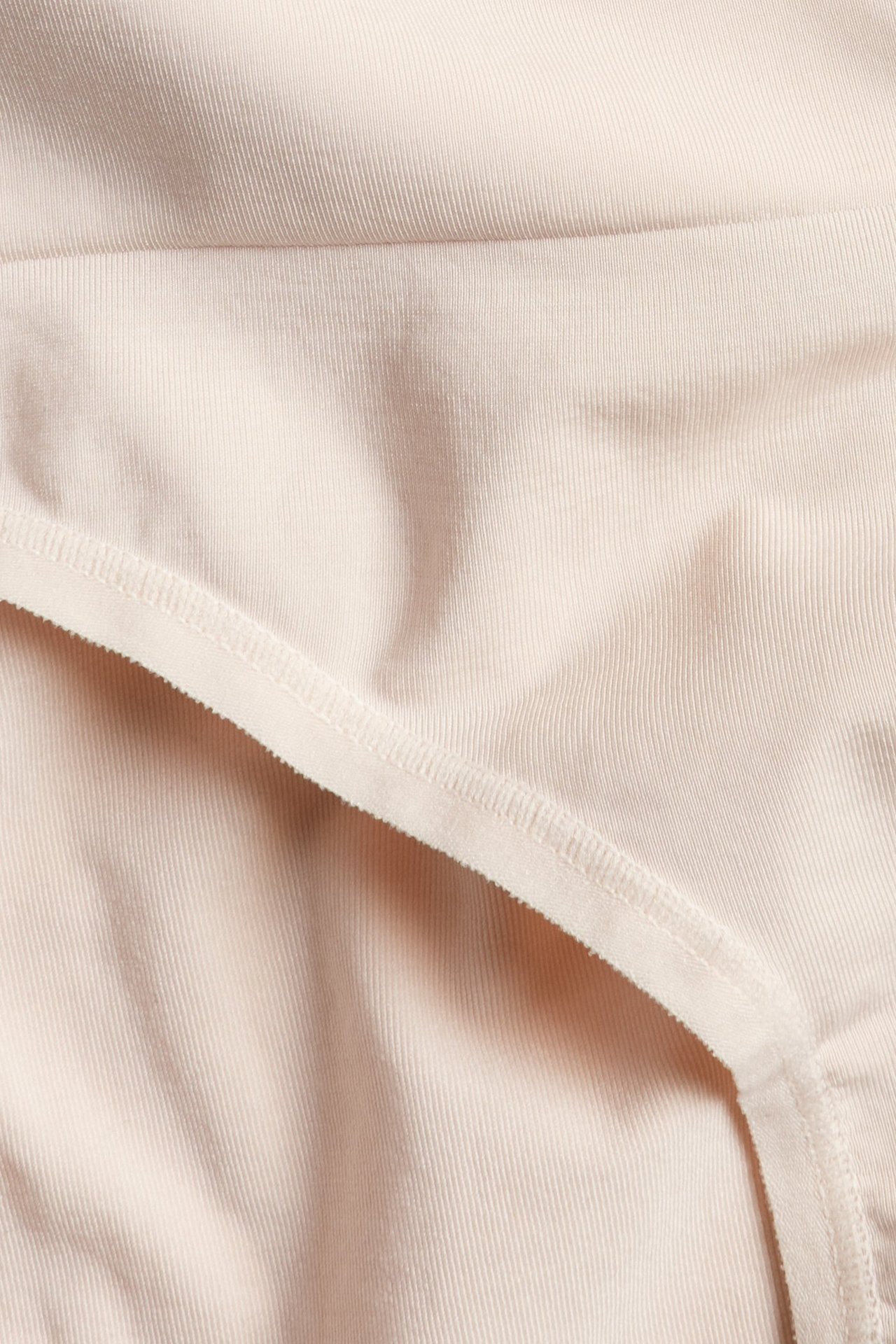 Zbliżenie jasnoróżowych majtek modelujących z prążkowaną fakturą i widocznymi szwami.