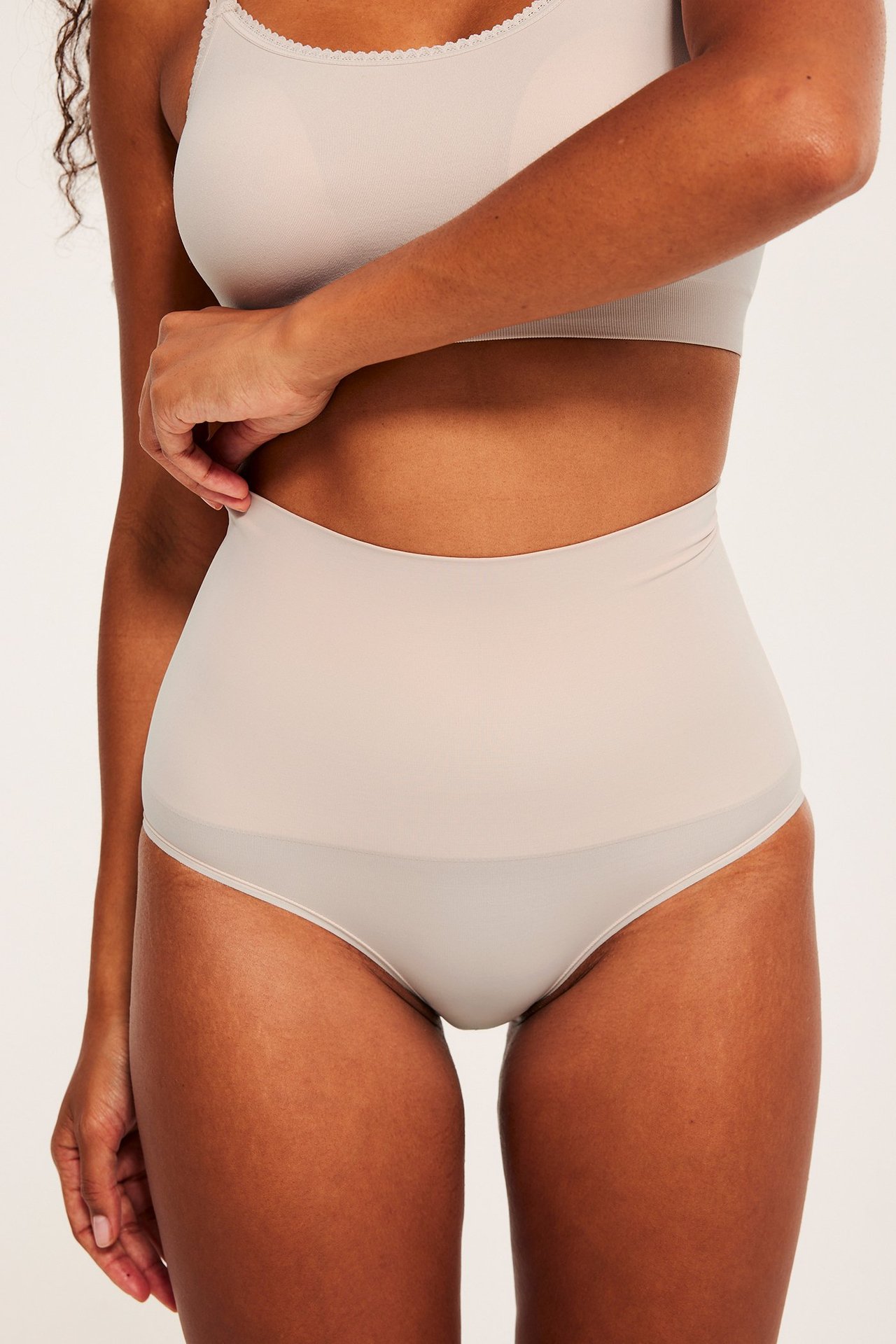 Frontbilde av en kvinne i lys rosa høy shapingtruse og matchende bralette.