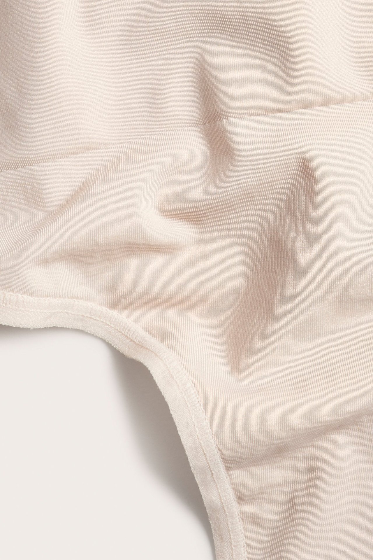 Zbliżenie na jasnoróżowe, jednolite stringi damskie z prążkowanej, elastycznej tkaniny.