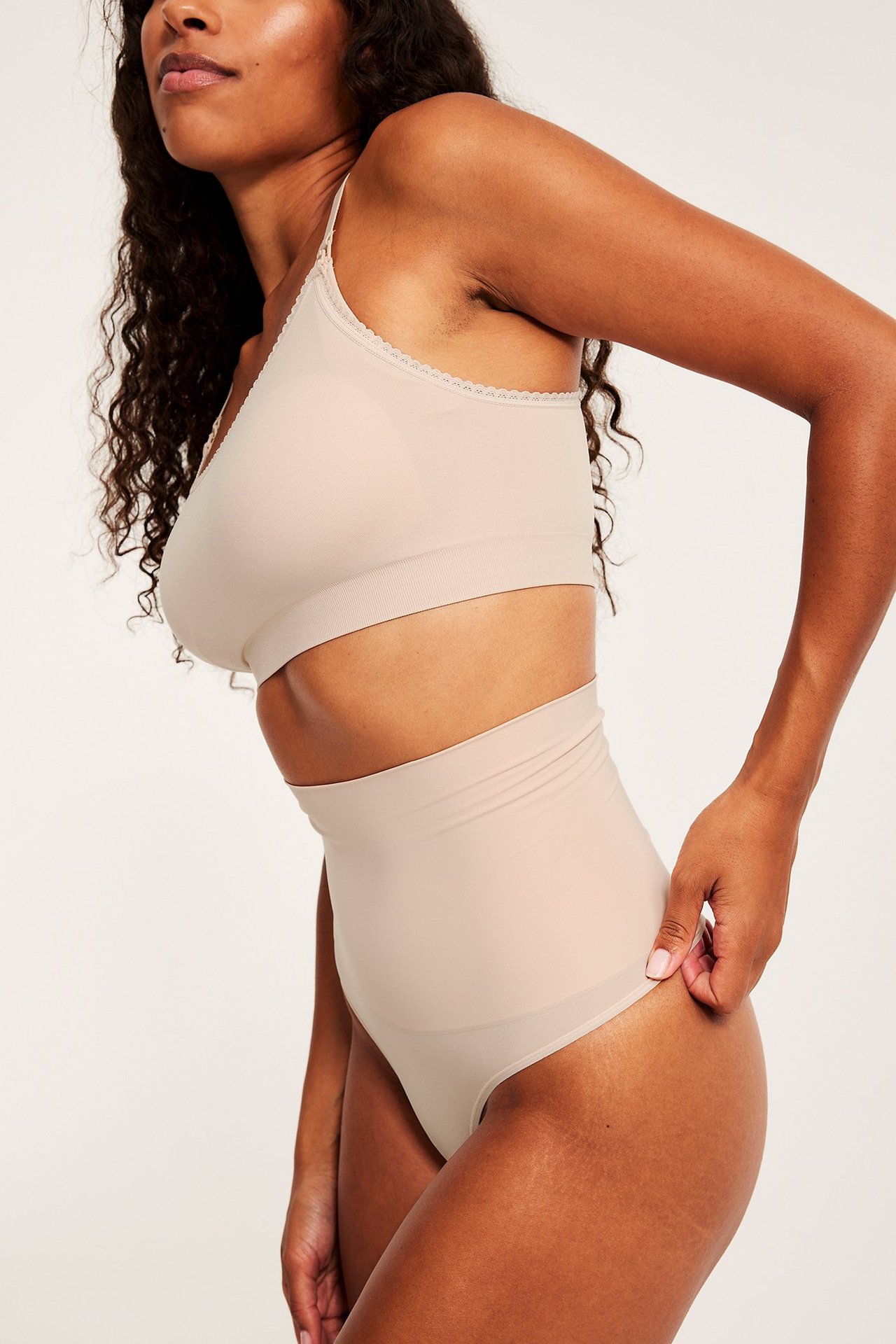 Sidebilde av en kvinne i lys rosa høytlivs shaping stringtruse og matchende bralette.