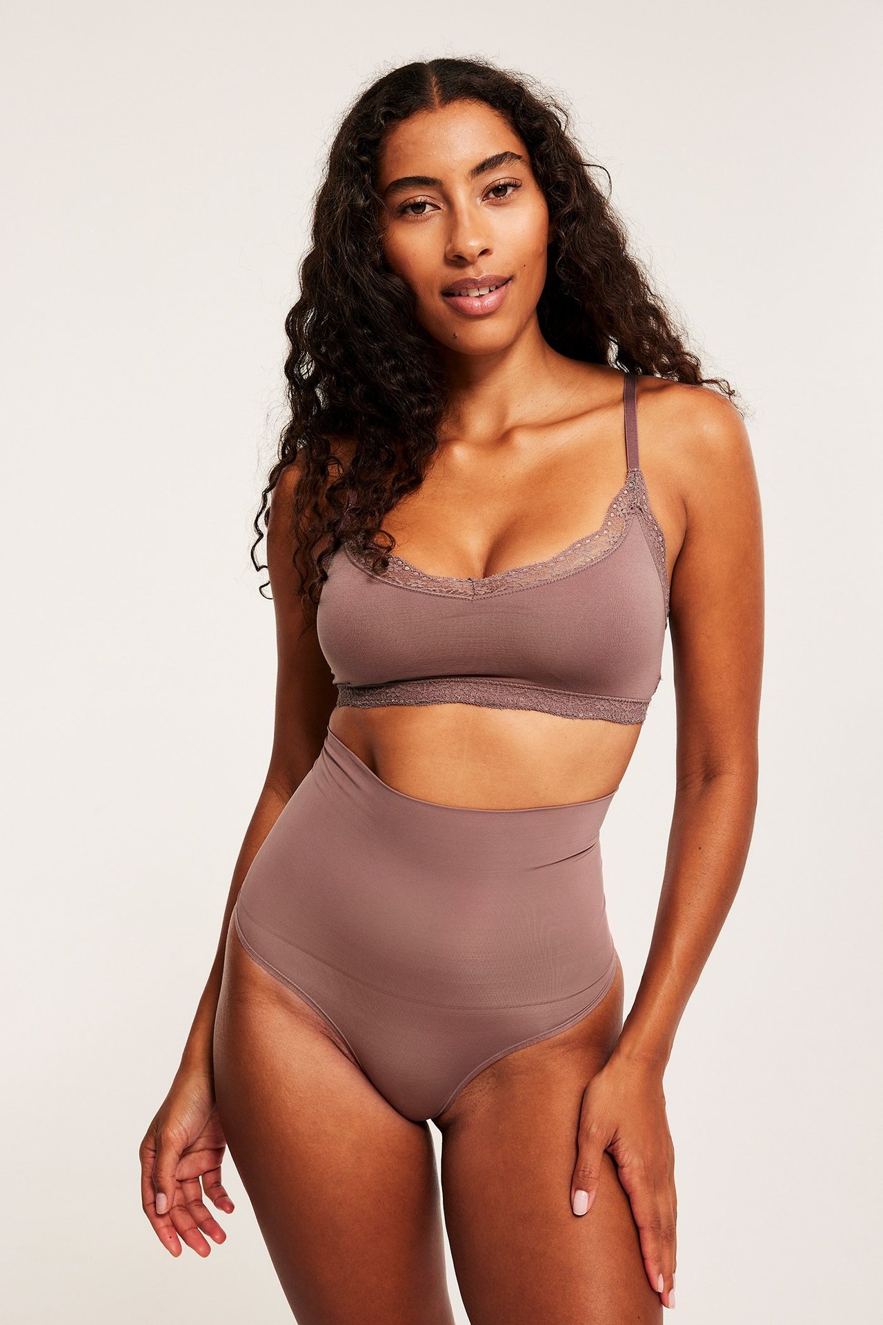 Frontbilde av en kvinne i mørk rosa høy midje shape string og matchende BH med blondekant.