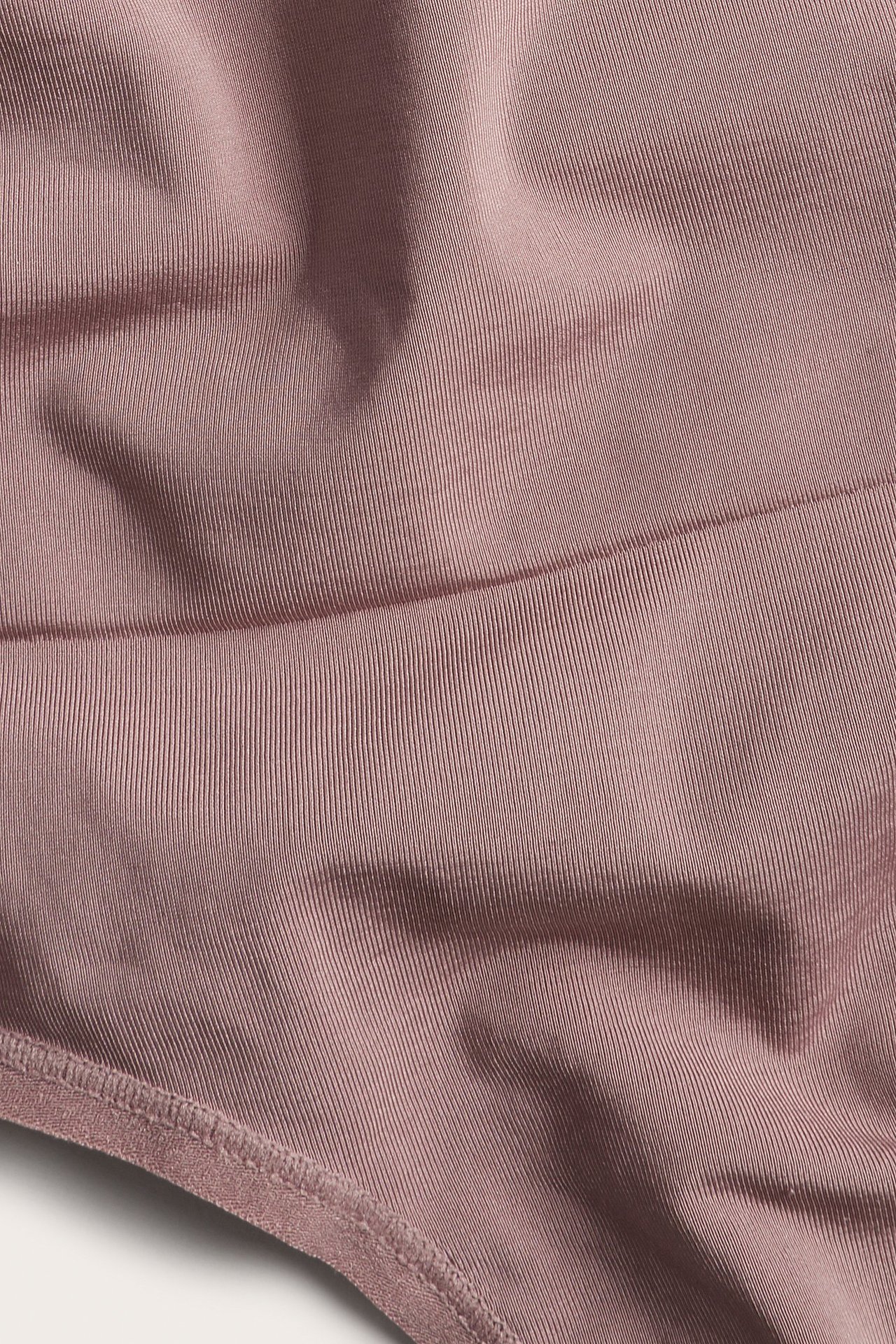 Zbliżenie na ciemnoróżowe prążkowane stringi modelujące z poliestru z recyklingu, widać fakturę i szwy.