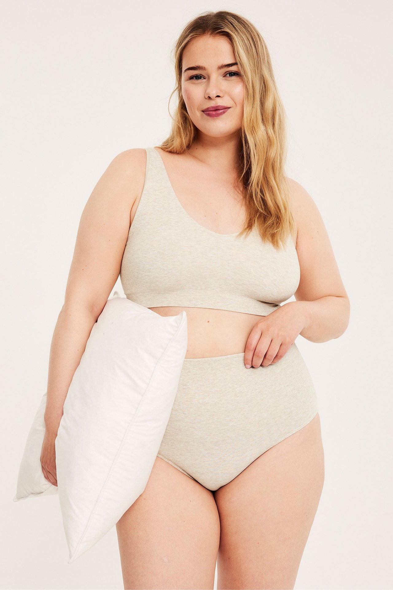 Framifrån, kvinna i melerad beige sömlös bomullsmix-bh och matchande trosa, håller en vit kudde.
