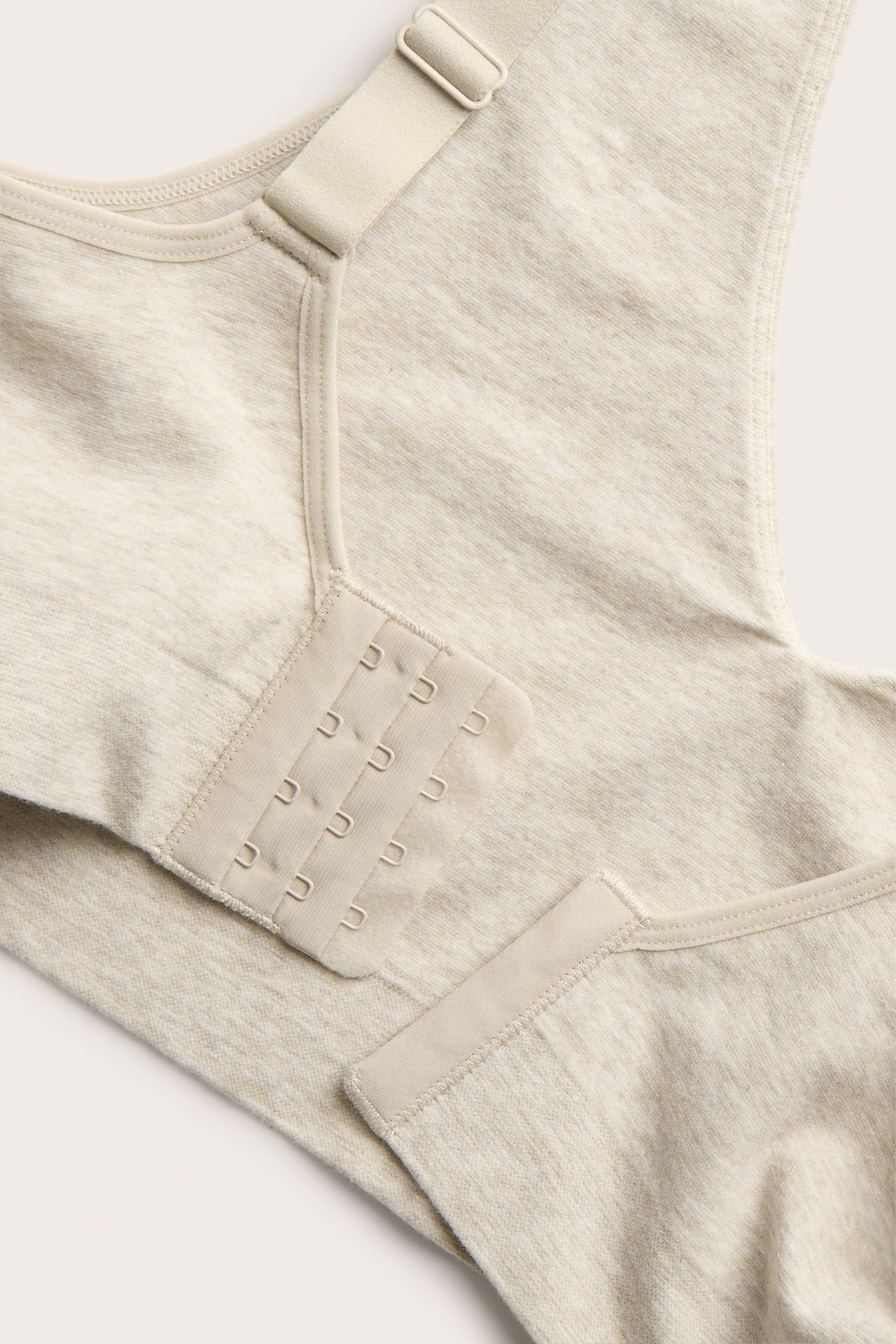 Zbliżenie beżowego melanżowego biustonosza bezszwowego z regulowanym ramiączkiem i zapięciem na haftki.