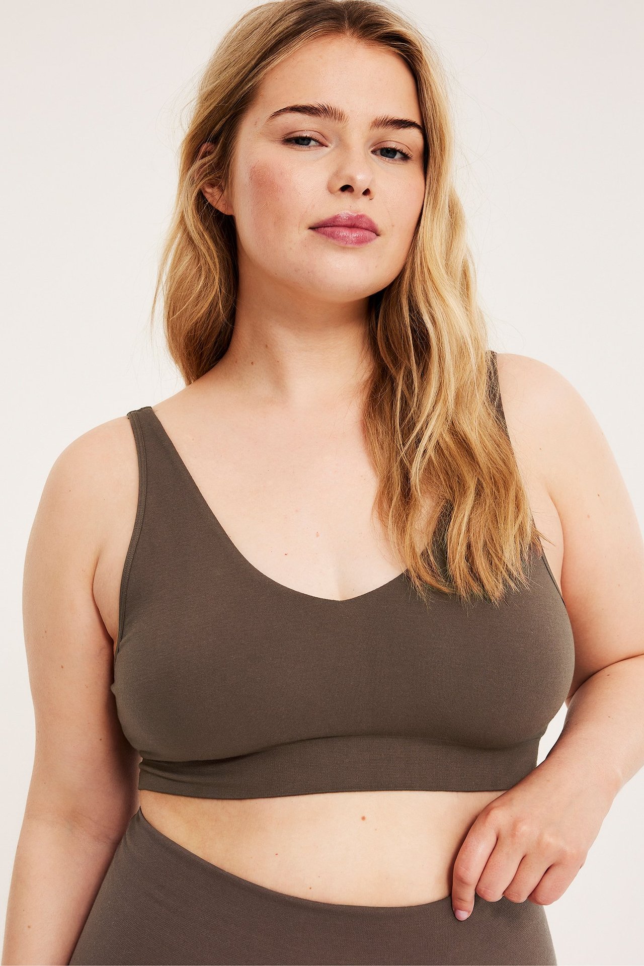 Närbild framifrån på en kvinna i en mörkbrun sömlös V-ringad BH och matchande underdel.