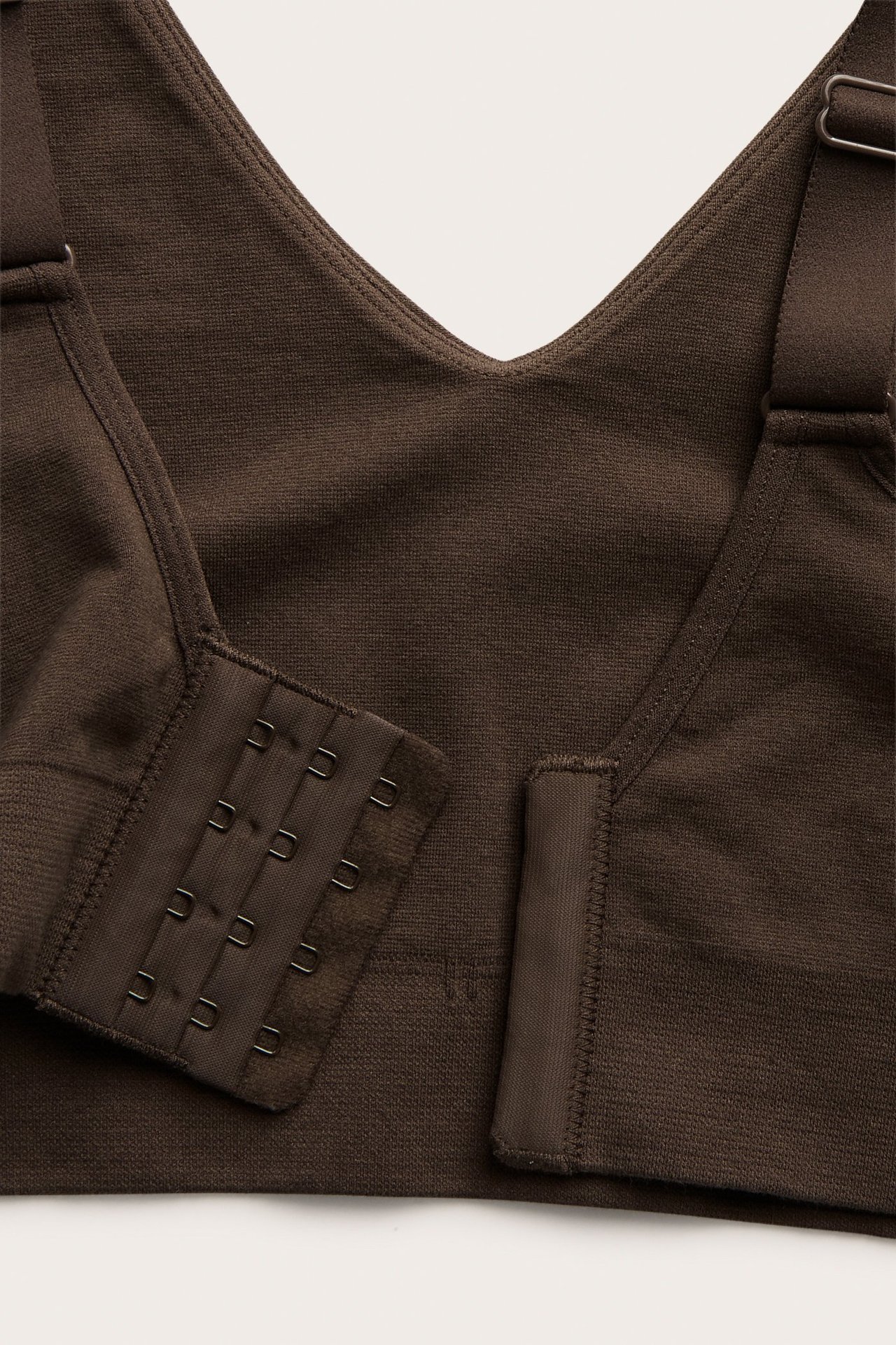 Zbliżenie: ciemnobrązowy, bezszwowy biustonosz z dekoltem w serek, ramiączkami i zapięciem na haftki.