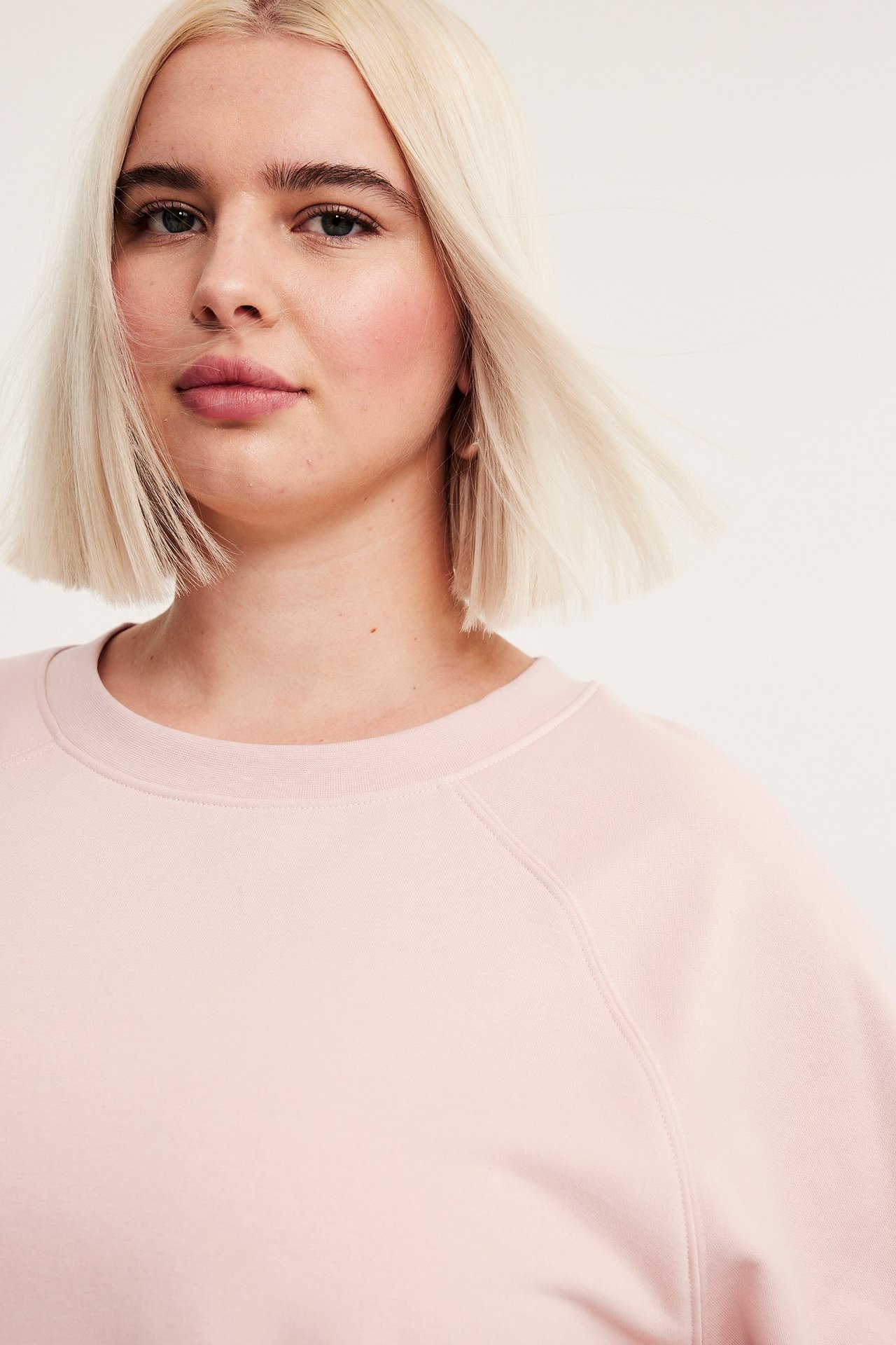 Närbild framifrån på en kvinna i en ljusrosa kortärmad sweatshirt i bomullsblandning.