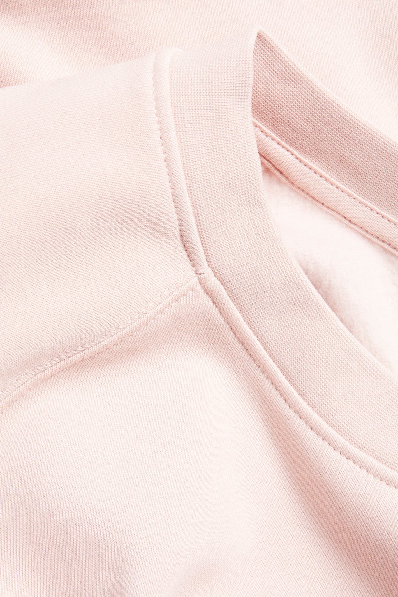Zbliżenie na jasnoróżową bluzę z krótkim rękawem, z prążkowanym kołnierzem i widocznymi szwami.
