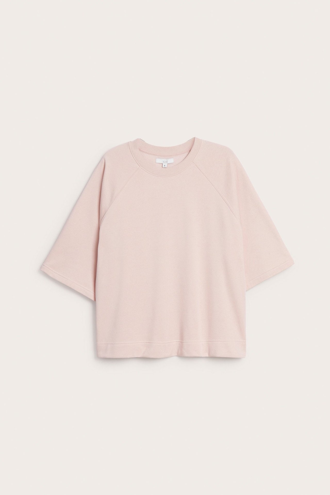 Widok z przodu jasnoróżowej, krótkiej bluzy z okrągłym dekoltem, wykonanej z mieszanki bawełny, o luźnym kroju.